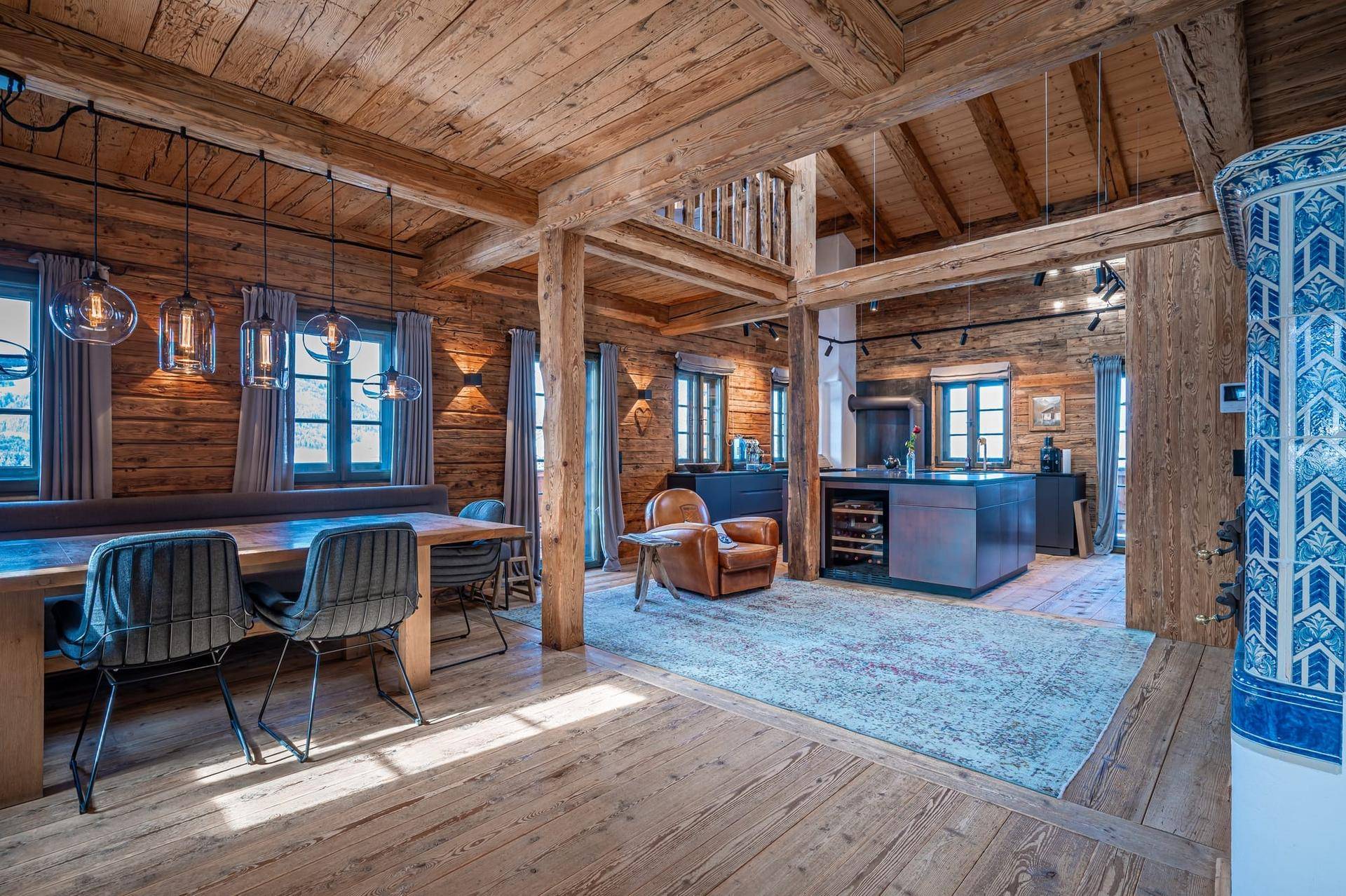 Offener Wohn- und Essbereich in einem Holzchalet mit modernem Küchenblock und traditionellem Kachelofen.