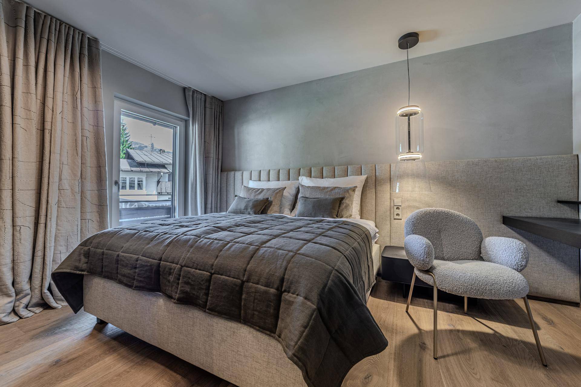 Helles Schlafzimmer mit Doppelbett, stilvollem Sessel und Zugang zu einem kleinen Balkon.