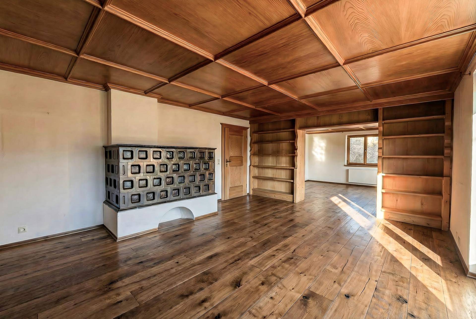 Geräumiges Wohnzimmer mit traditionellem Kachelofen, Holzboden und eingebauten Bücherregalen.