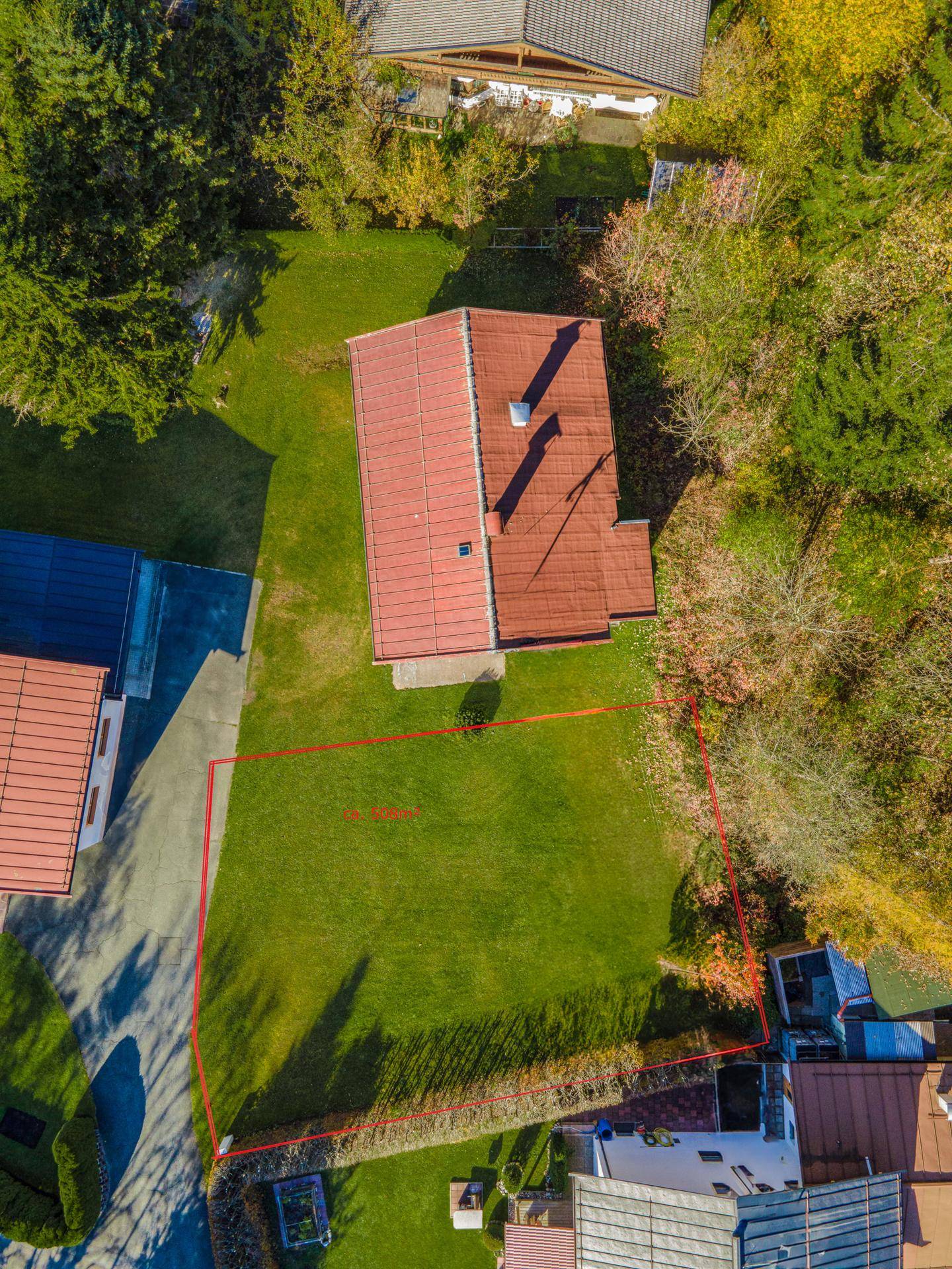 Luftaufnahme eines Grundstücks mit Wohnhaus und Rasenfläche, umrandet von Bäumen und Nachbargebäuden.