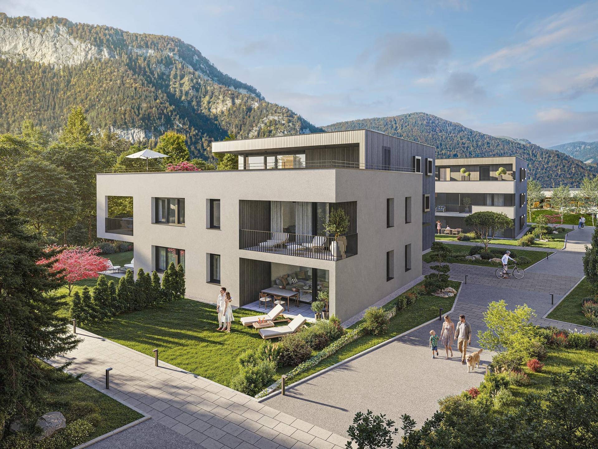 Moderne Wohnanlage mit weitläufigen Grünflächen, Liegestühlen und beeindruckendem Bergblick.