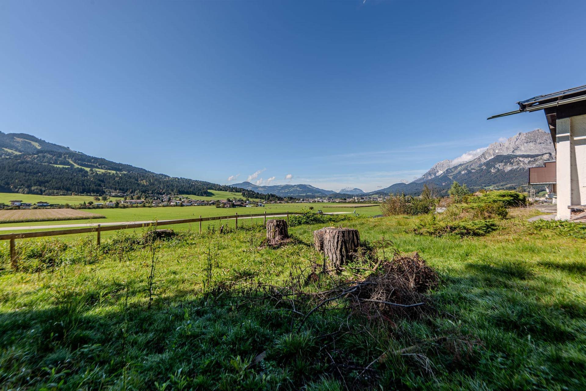 Weitläufige grüne Landschaft mit Blick auf die Berge und ein angrenzendes Gebäude unter blauem Himmel.