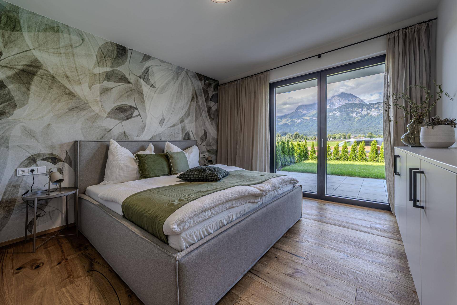 Gemütliches Schlafzimmer mit floraler Tapete, Holzboden und direktem Zugang zur Terrasse mit Bergblick.