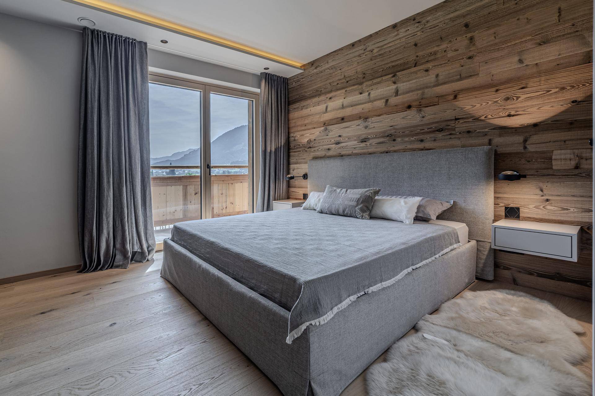 Gemütliches Schlafzimmer mit Holzwand, Parkettboden und direktem Zugang zu einem Balkon mit Bergblick.