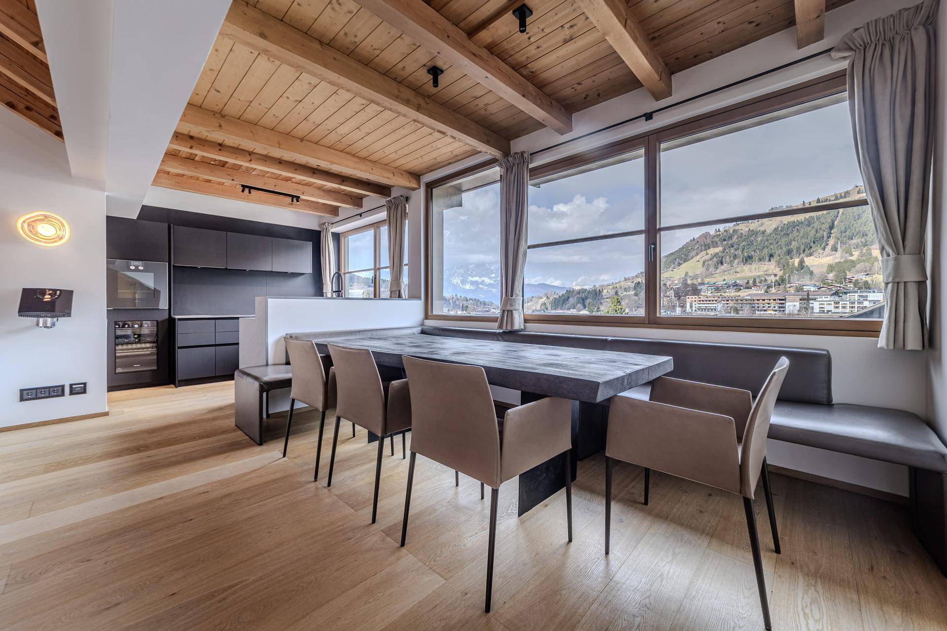 Moderner Essbereich mit Holzbalkendecke, integrierter Sitzbank und Panoramablick auf die Berge.