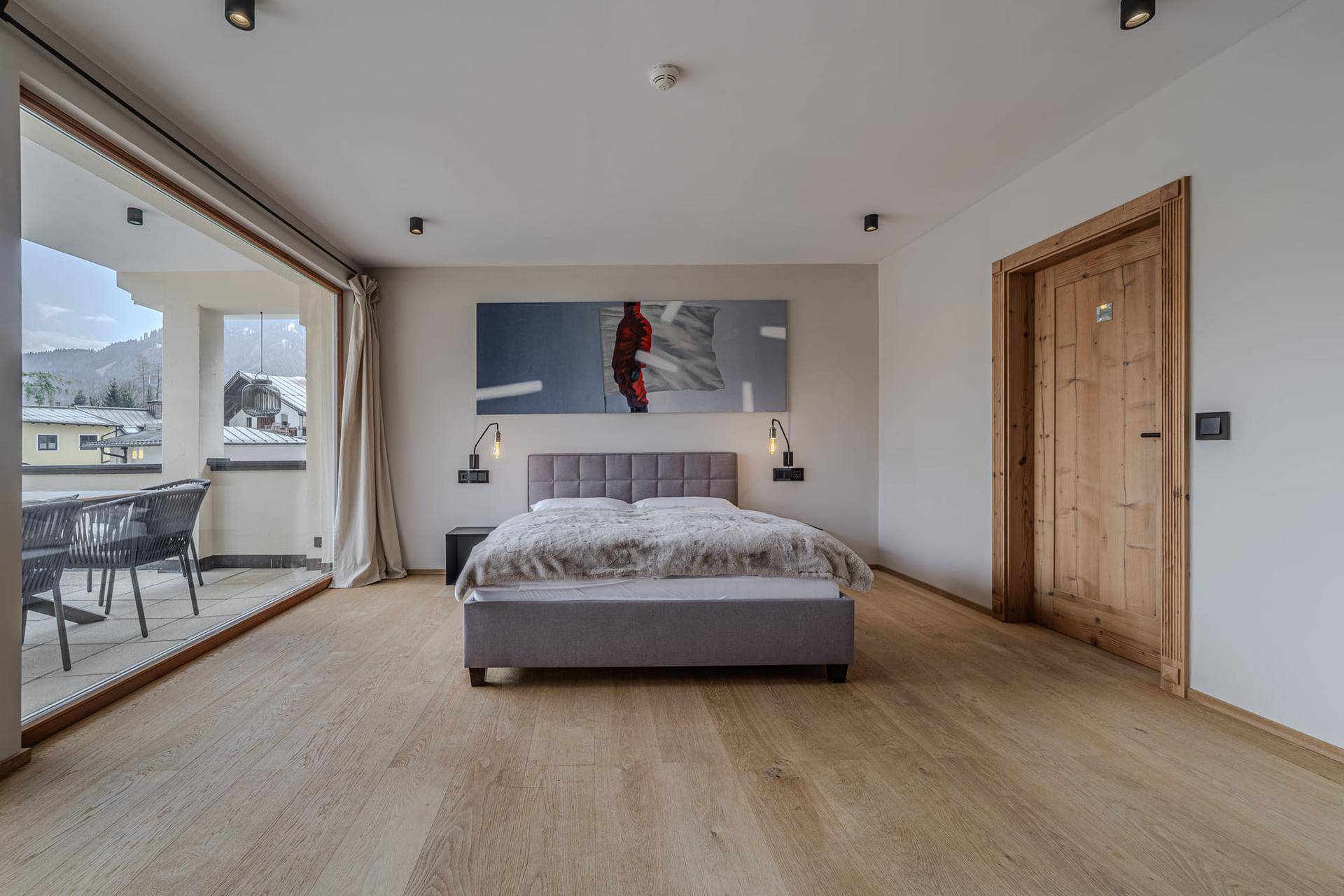 Helles Schlafzimmer mit Holzboden, Zugang zu einem Balkon und moderner Einrichtung.
