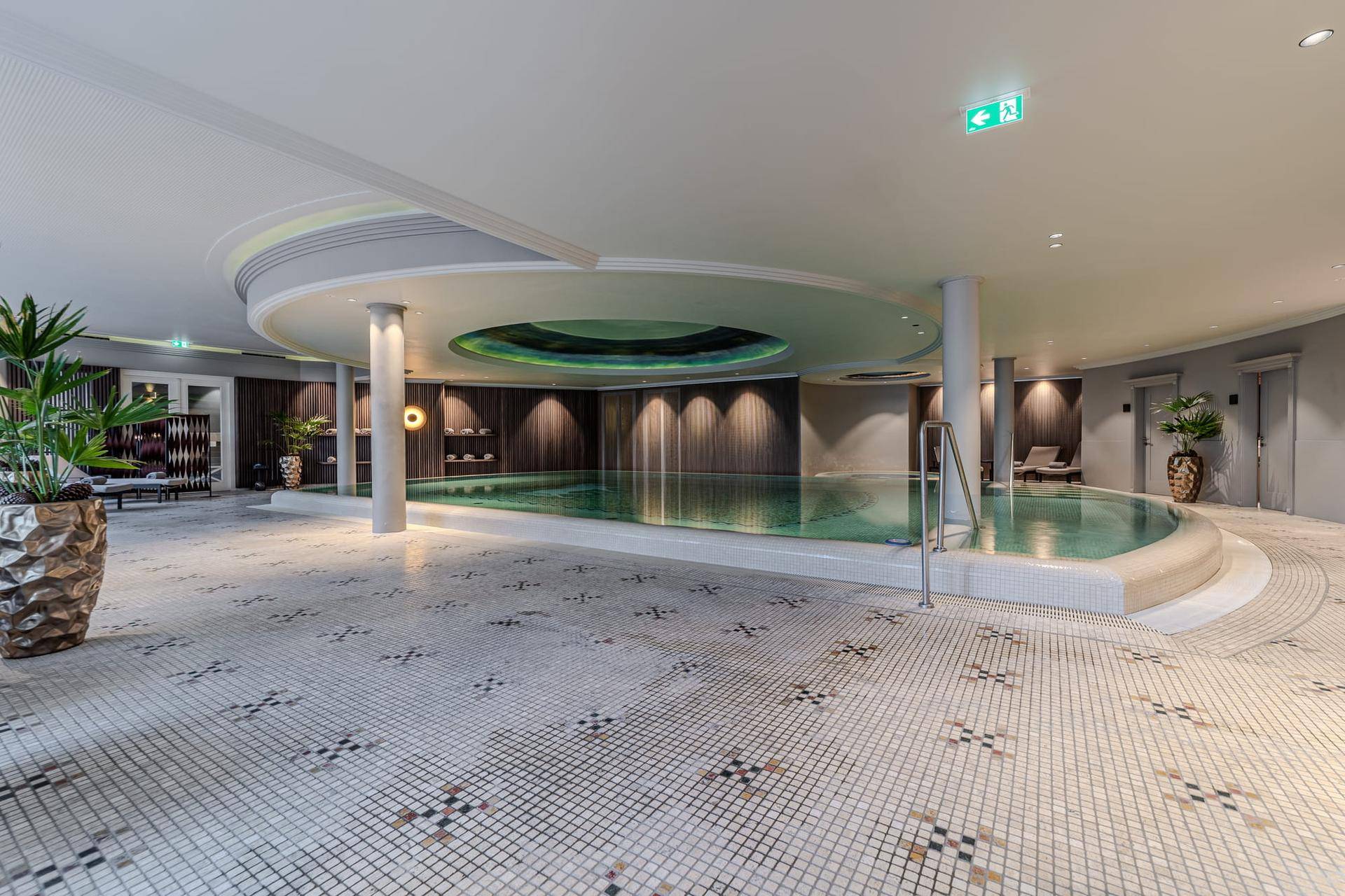 Elegantes Hallenbad mit Mosaikfliesen und stilvoller Beleuchtung in einem Wellnessbereich.