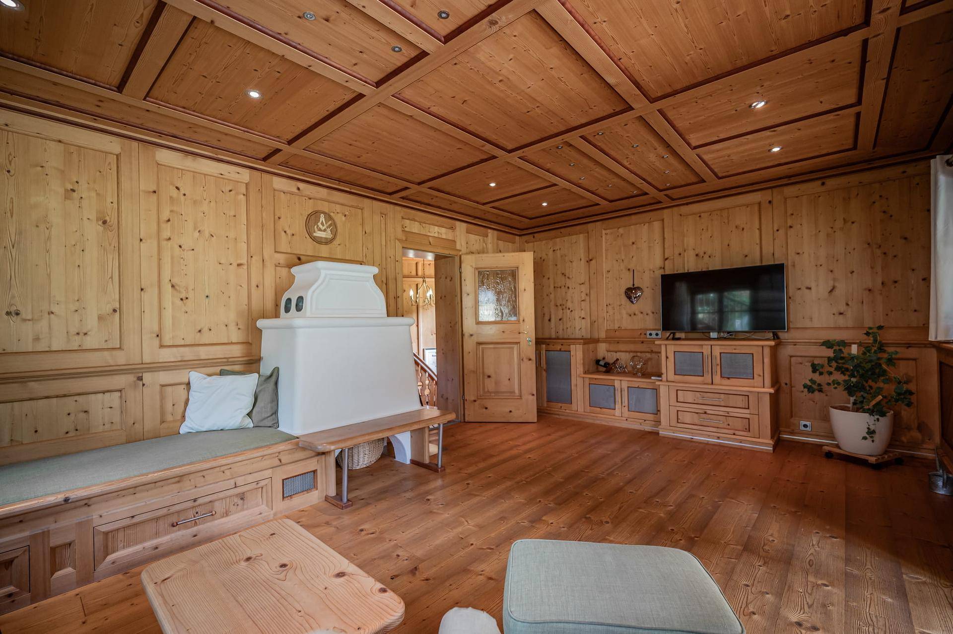 Gemütliches Wohnzimmer mit aufwendiger Holzvertäfelung, Kassettendecke und einem traditionellen Kachelofen.