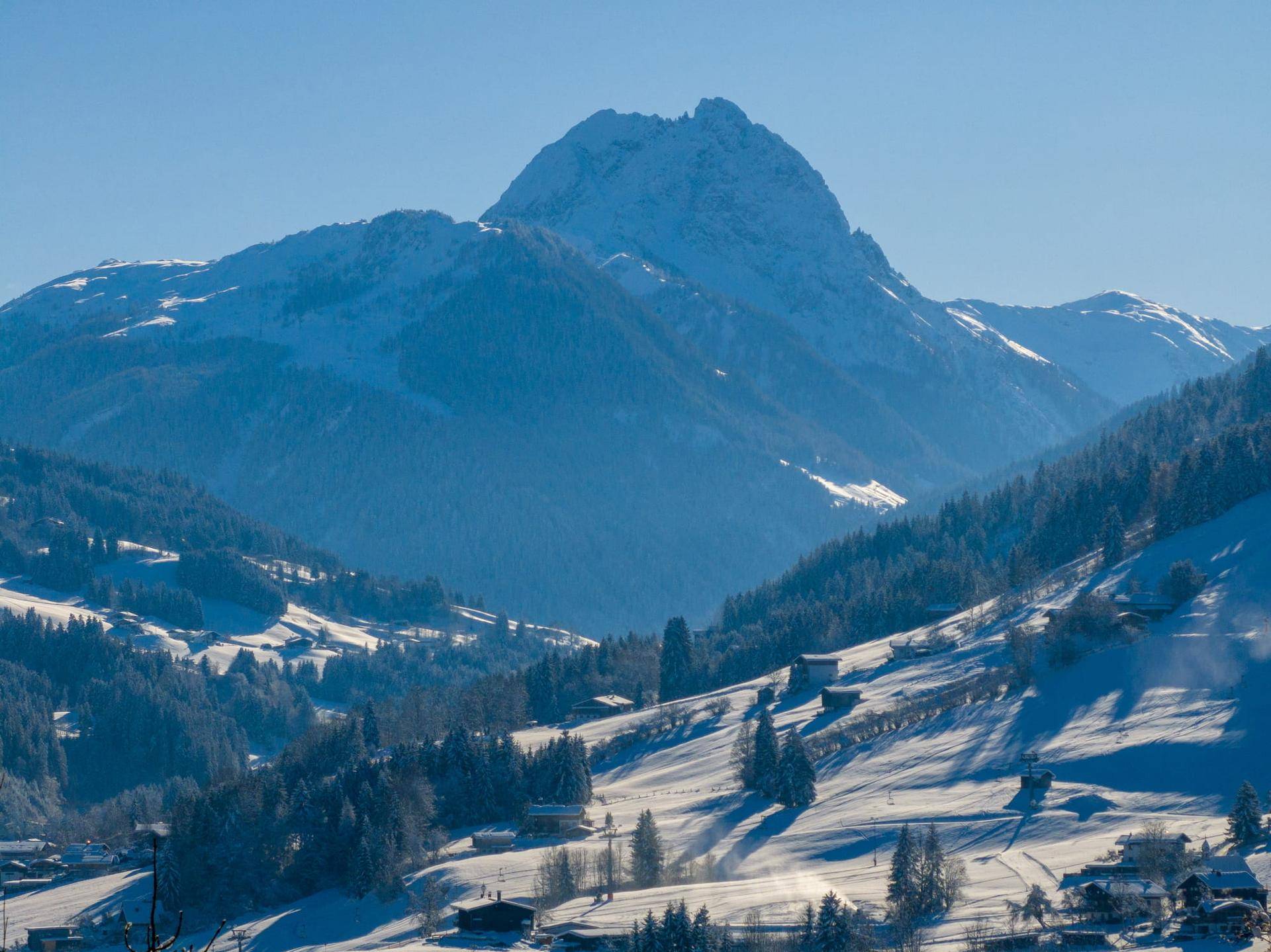 Majestätischer schneebedeckter Berggipfel über einem Tal mit verstreuten Häusern und Wäldern.