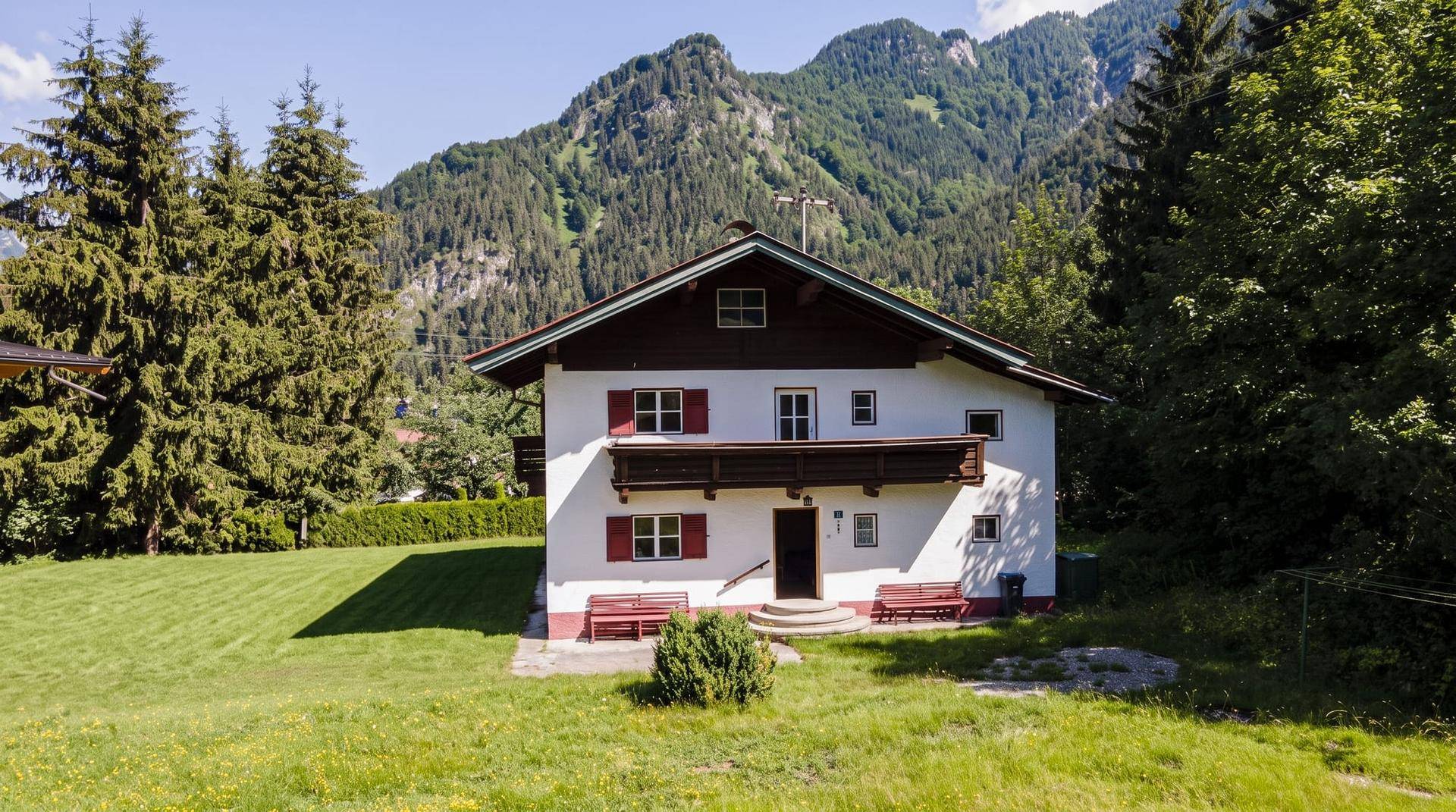 Traditionelles Alpenhaus mit weißer Fassade, roten Fensterläden und Bergblick.