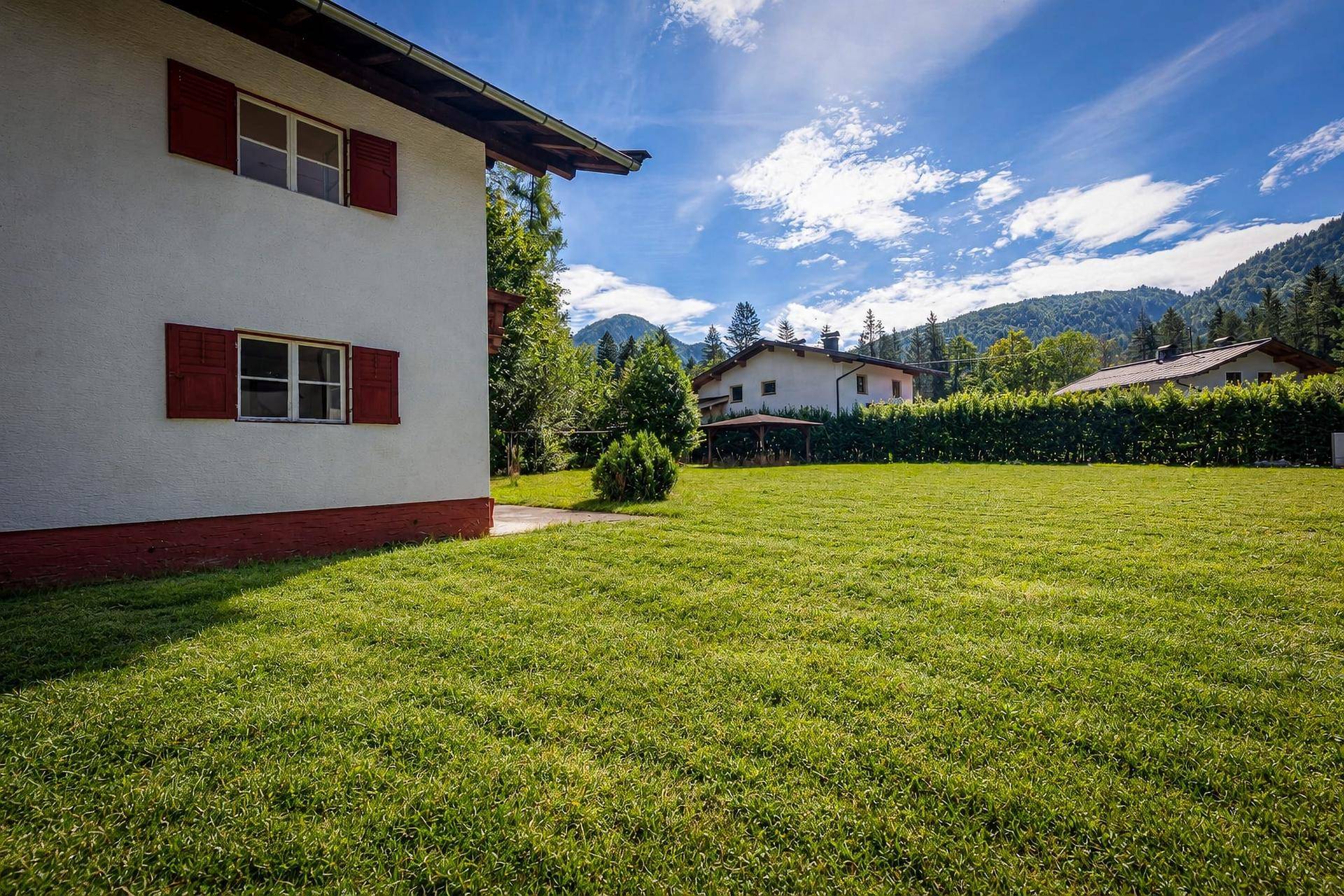 Seitenansicht des Hauses mit gepflegtem Rasen, einer Hecke und Bergblick im Hintergrund.