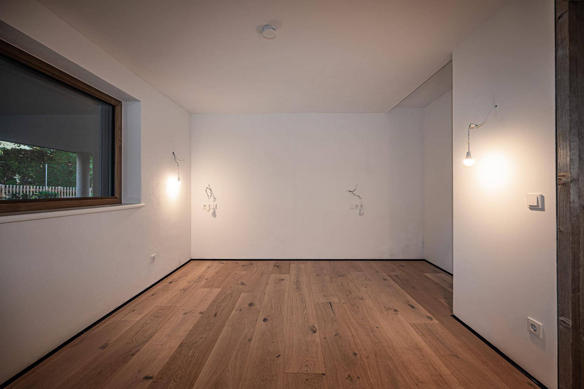 Helles Schlafzimmer mit Holzboden und einem Fenster, das viel Tageslicht hereinlässt.
