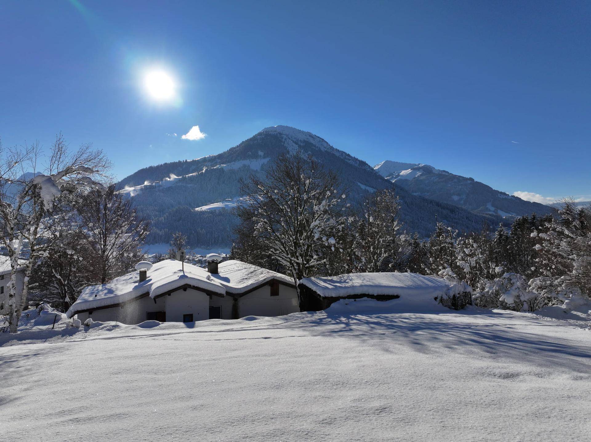 Winterliche Landschaft mit verschneiten Häusern und majestätischem Bergpanorama unter strahlendem Himmel.