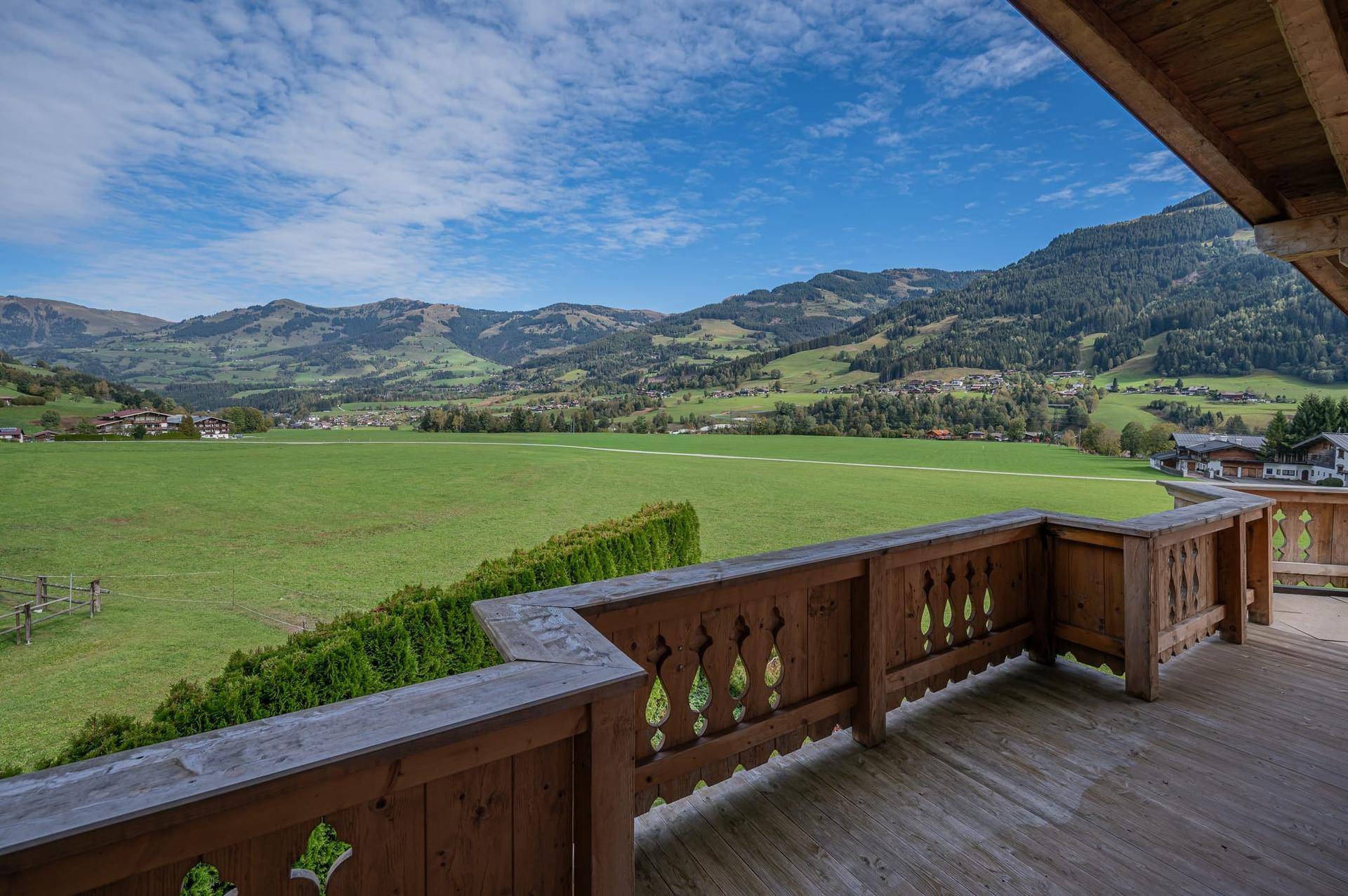 Großer Holzbalkon mit traditionellem Geländer und weitem Blick über grüne Wiesen und Berge.