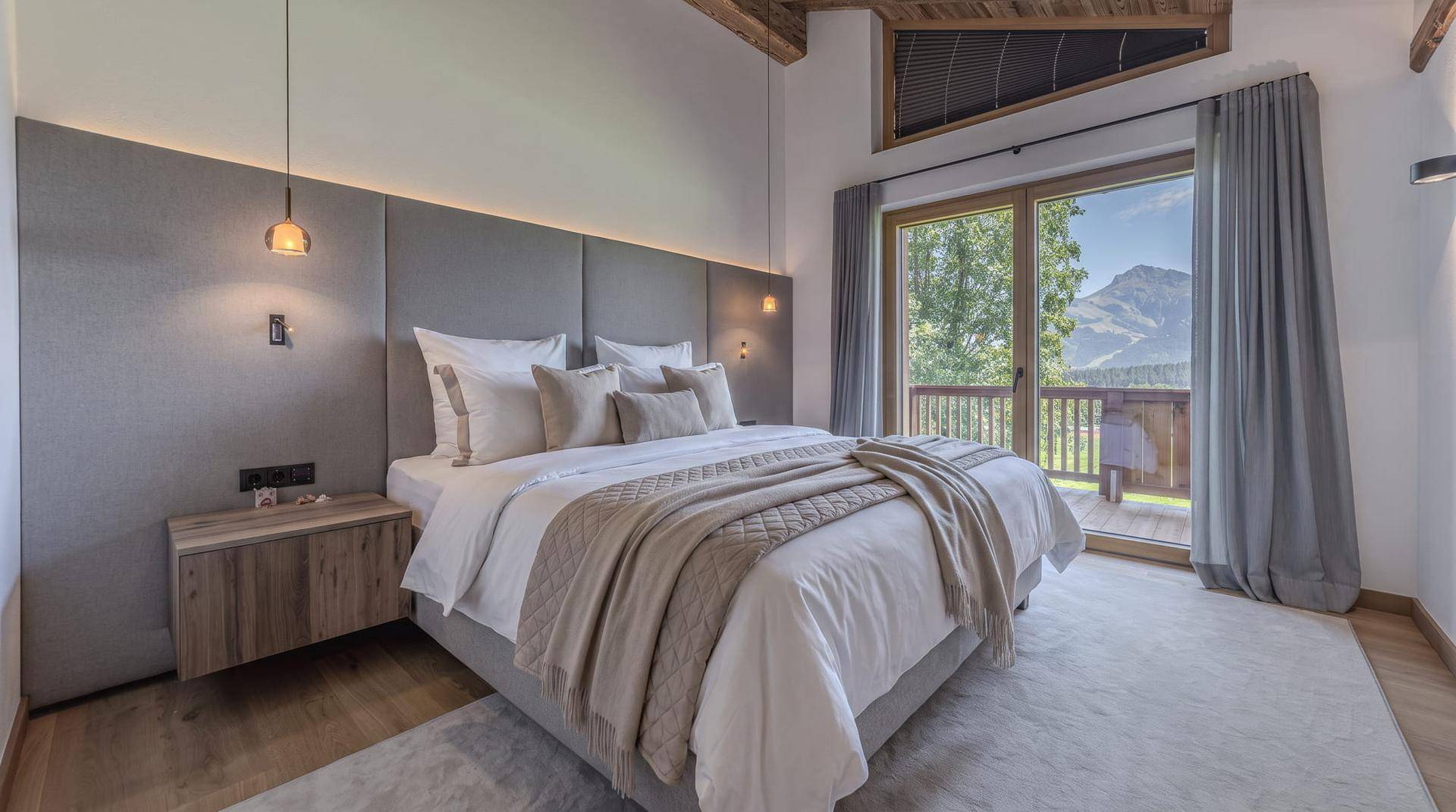 Gemütliches Schlafzimmer mit Holzbalkendecke, Balkonzugang und weitem Blick auf die umliegenden Berge.