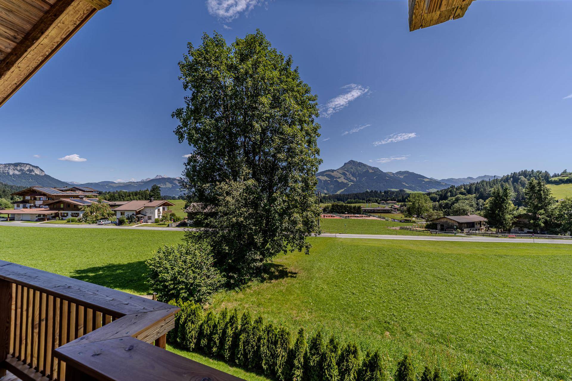 Panoramablick vom Balkon über grüne Wiesen und die umliegende Berglandschaft unter blauem Himmel.