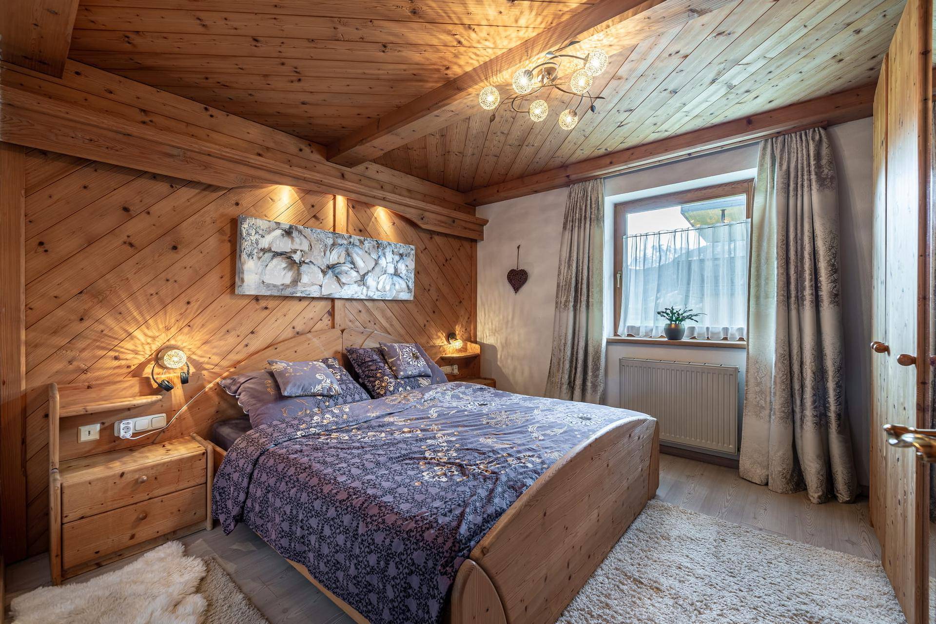 Gemütliches Schlafzimmer mit Holztäfelung, Doppelbett und Blick auf die Berge.