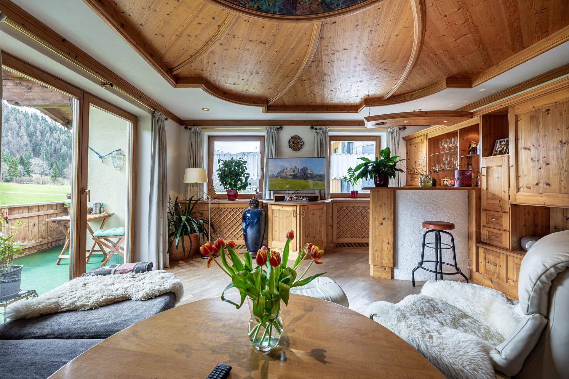 Helles Wohnzimmer mit Holzeinbauten, Zugang zum Balkon und weitem Blick auf die Landschaft.