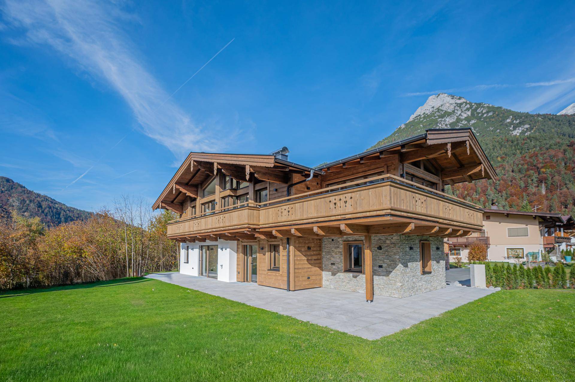 Modernes Chalet-Haus mit Holzbalkonen und Steinfassade vor einer beeindruckenden Bergkulisse.