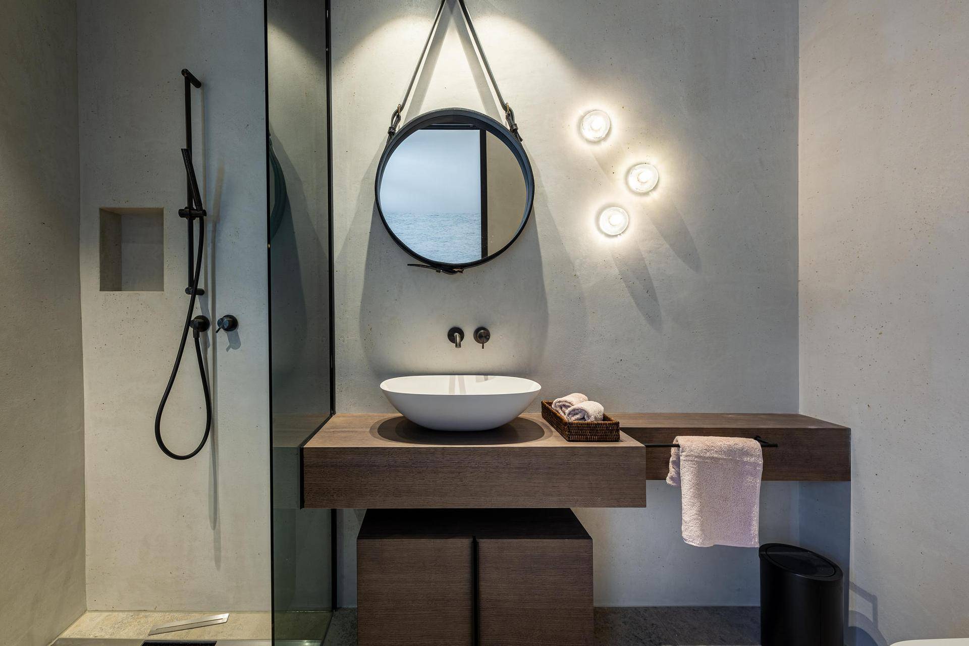 Modernes Badezimmer mit begehbarer Dusche, stilvollem Waschbecken und rundem Spiegel.
