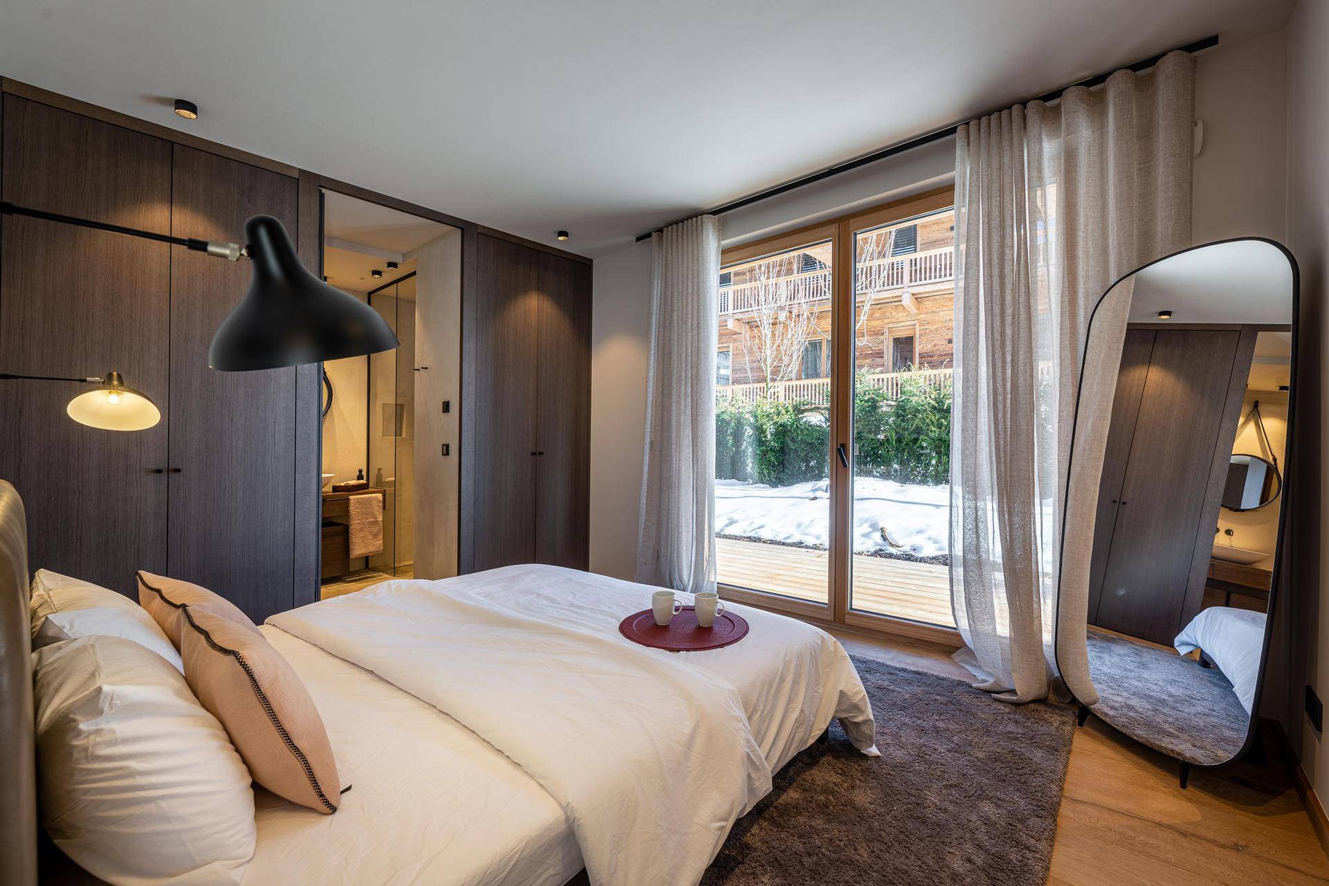 Gemütliches Schlafzimmer mit großem Bett, Einbauschränken und Zugang zu einem verschneiten Außenbereich.