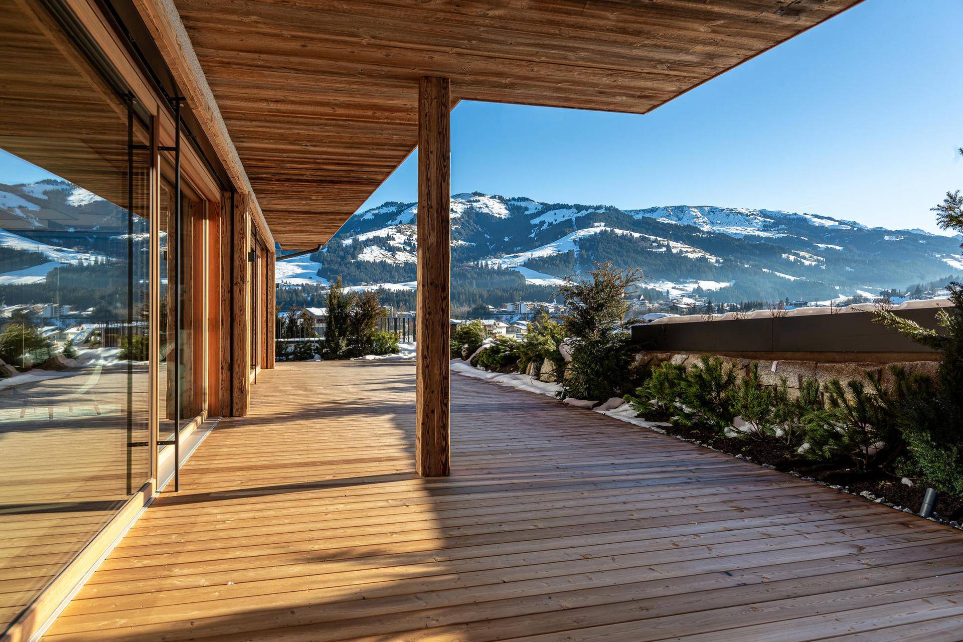 Geräumige Holzterrasse mit Panoramablick auf die verschneite Berglandschaft und großen Glasfronten.