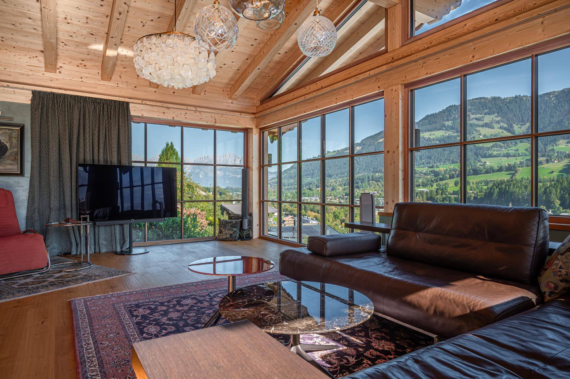Helles Wohnzimmer mit Holzbalkendecke, großen Fenstern und gemütlicher Ledercouch mit Bergblick.