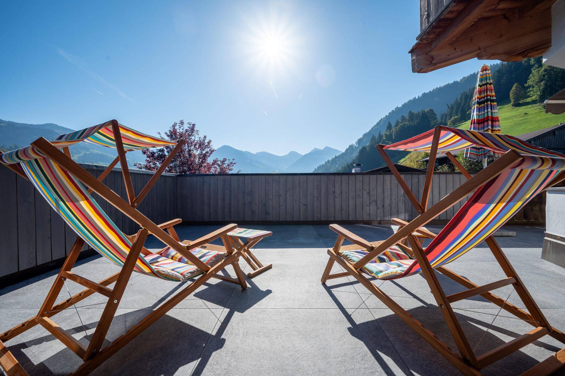 Sonniger Terrassenbereich mit bunten Liegestühlen und Panoramablick auf die umliegende Berglandschaft.
