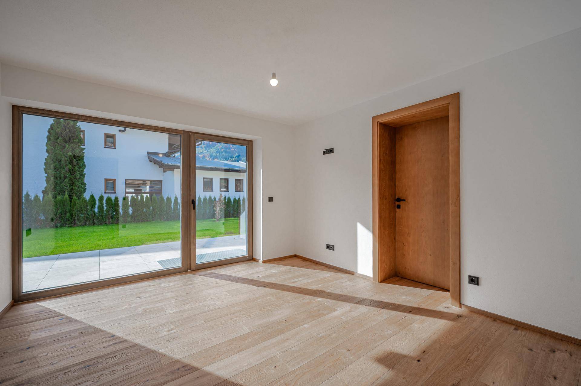 Heller Raum mit großen Fenstern, Holzboden und Blick ins Grüne.