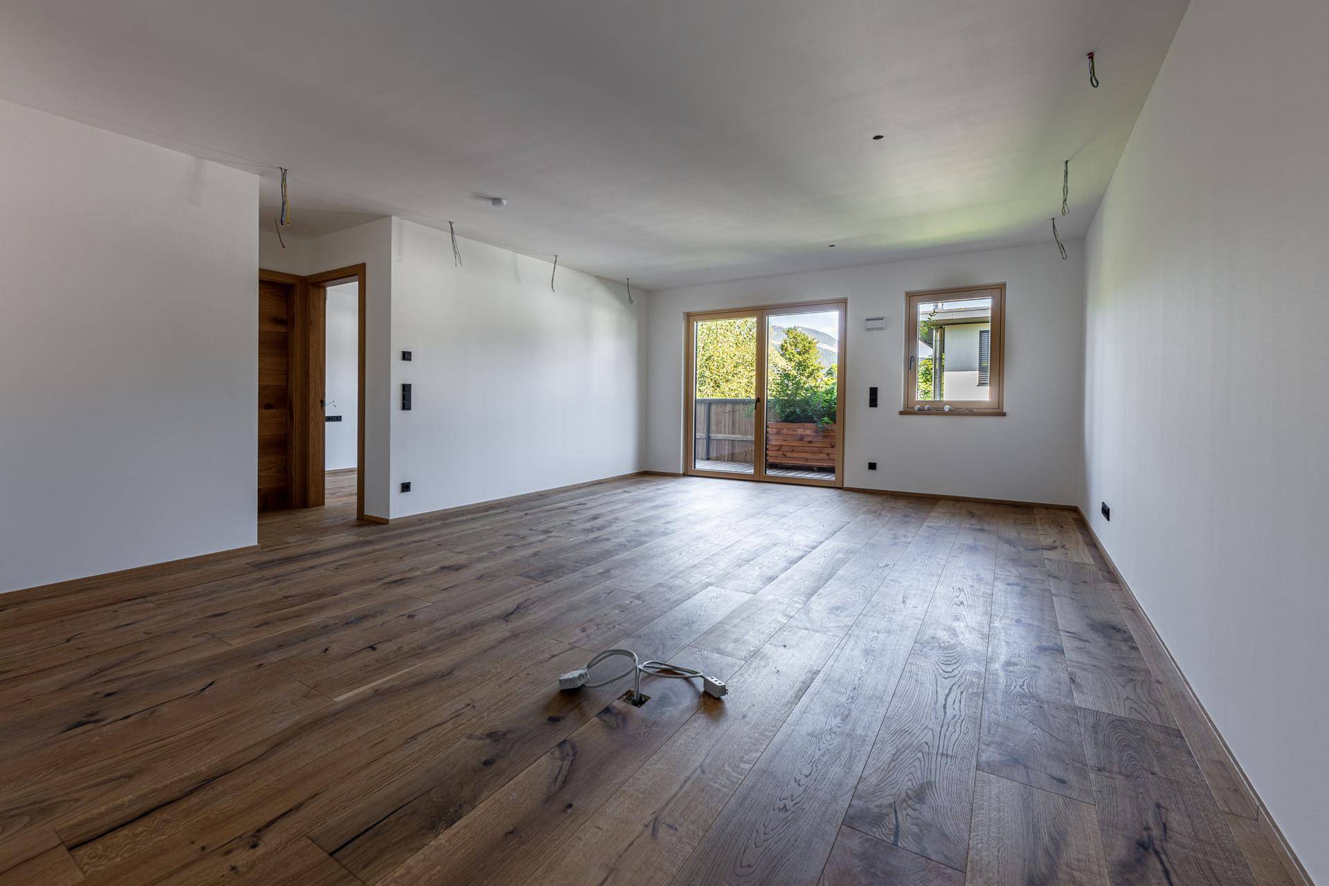 Heller, unmöblierter Wohnraum mit hochwertigem Holzboden und Zugang zum Balkon.