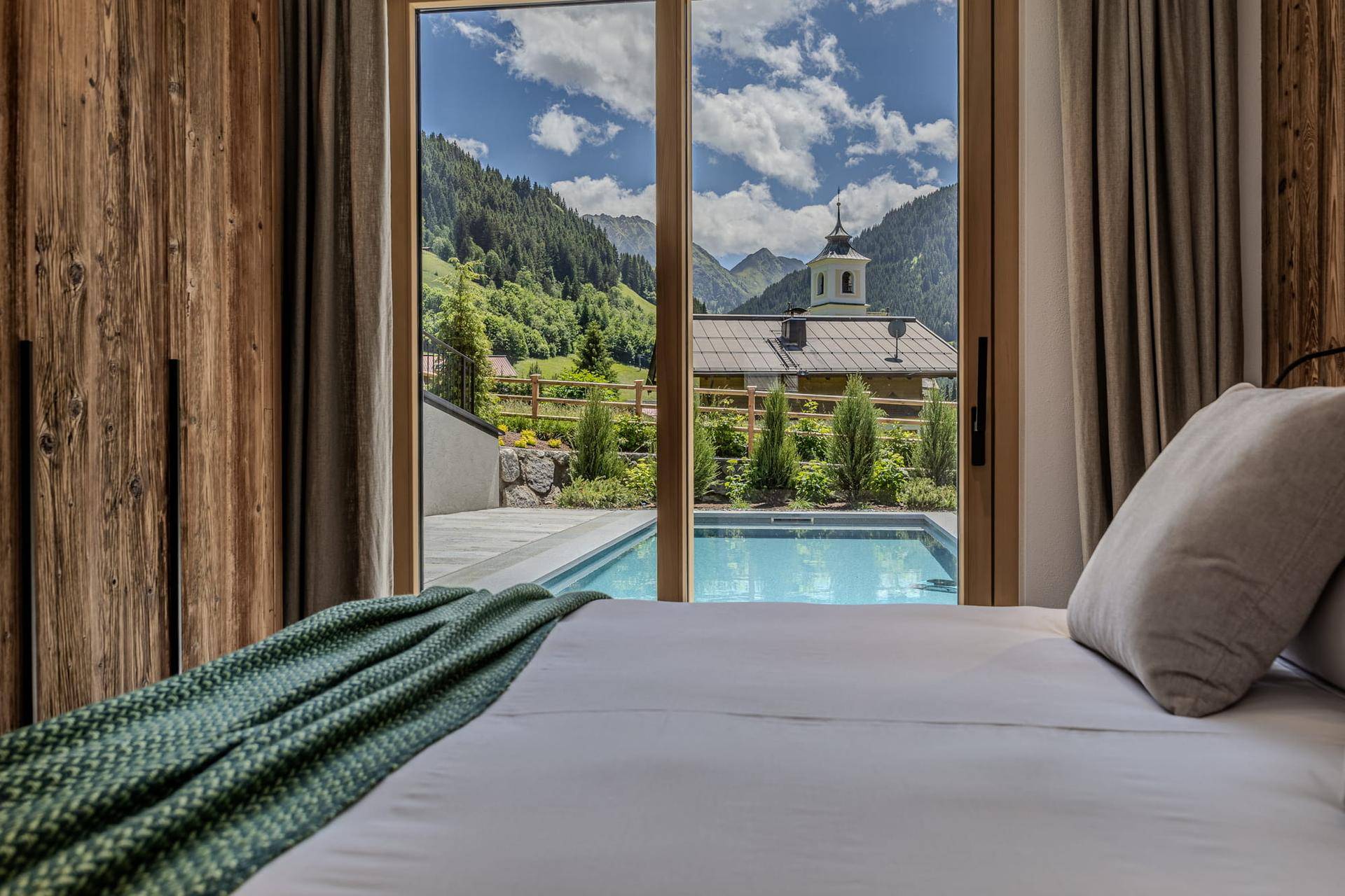 Schlafzimmer mit direktem Blick auf den Pool, die Berge und ein charmantes Dorfgebäude.