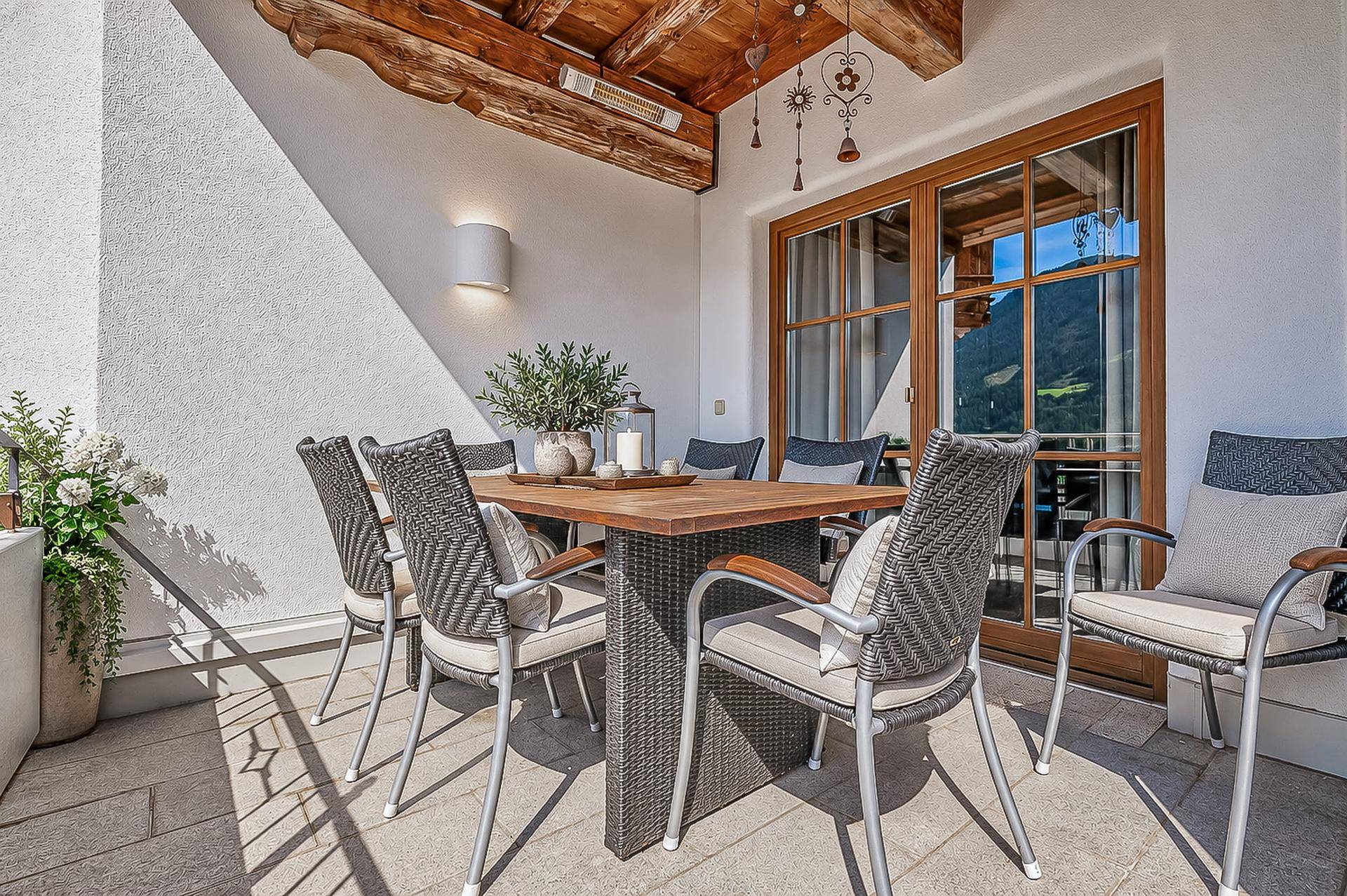 Sonnige Terrasse mit Esstisch und Stühlen, umgeben von alpiner Berglandschaft.