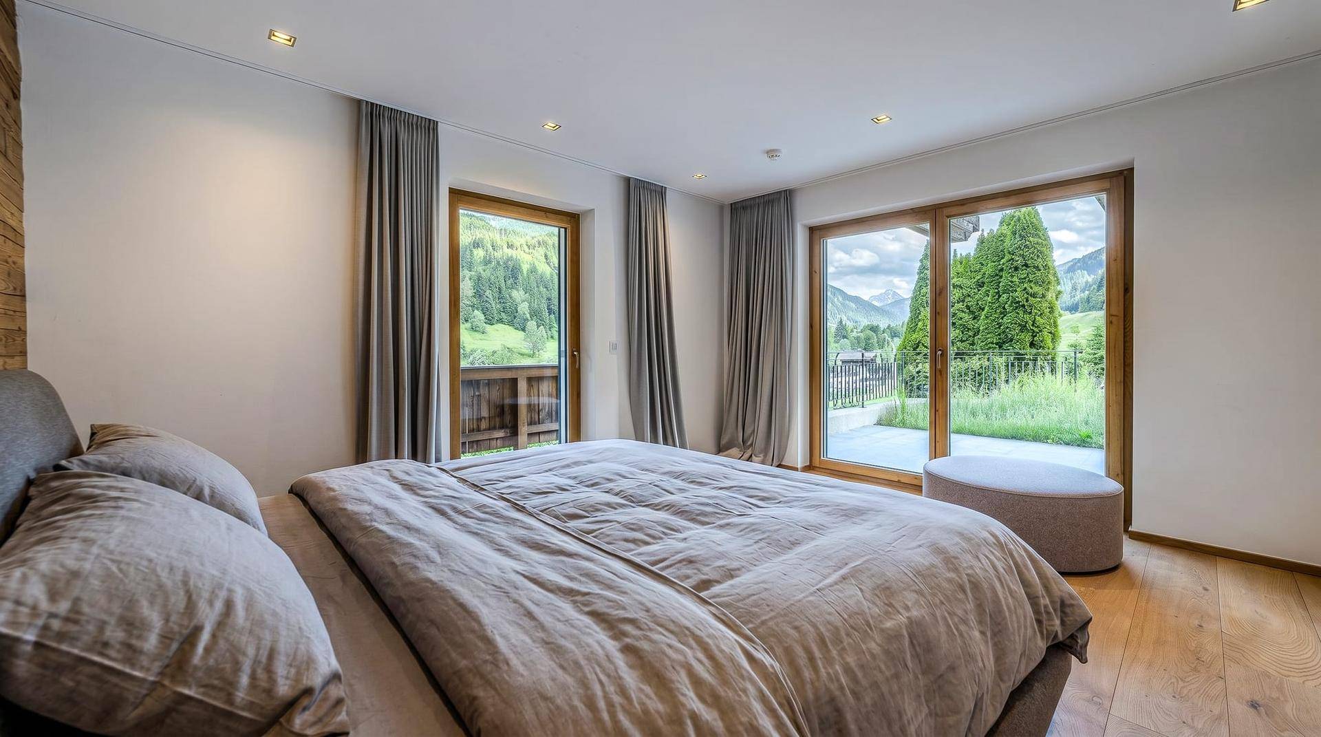 Helles Schlafzimmer mit Holzboden, großen Fenstern und direktem Zugang zu einem Balkon mit Bergblick.