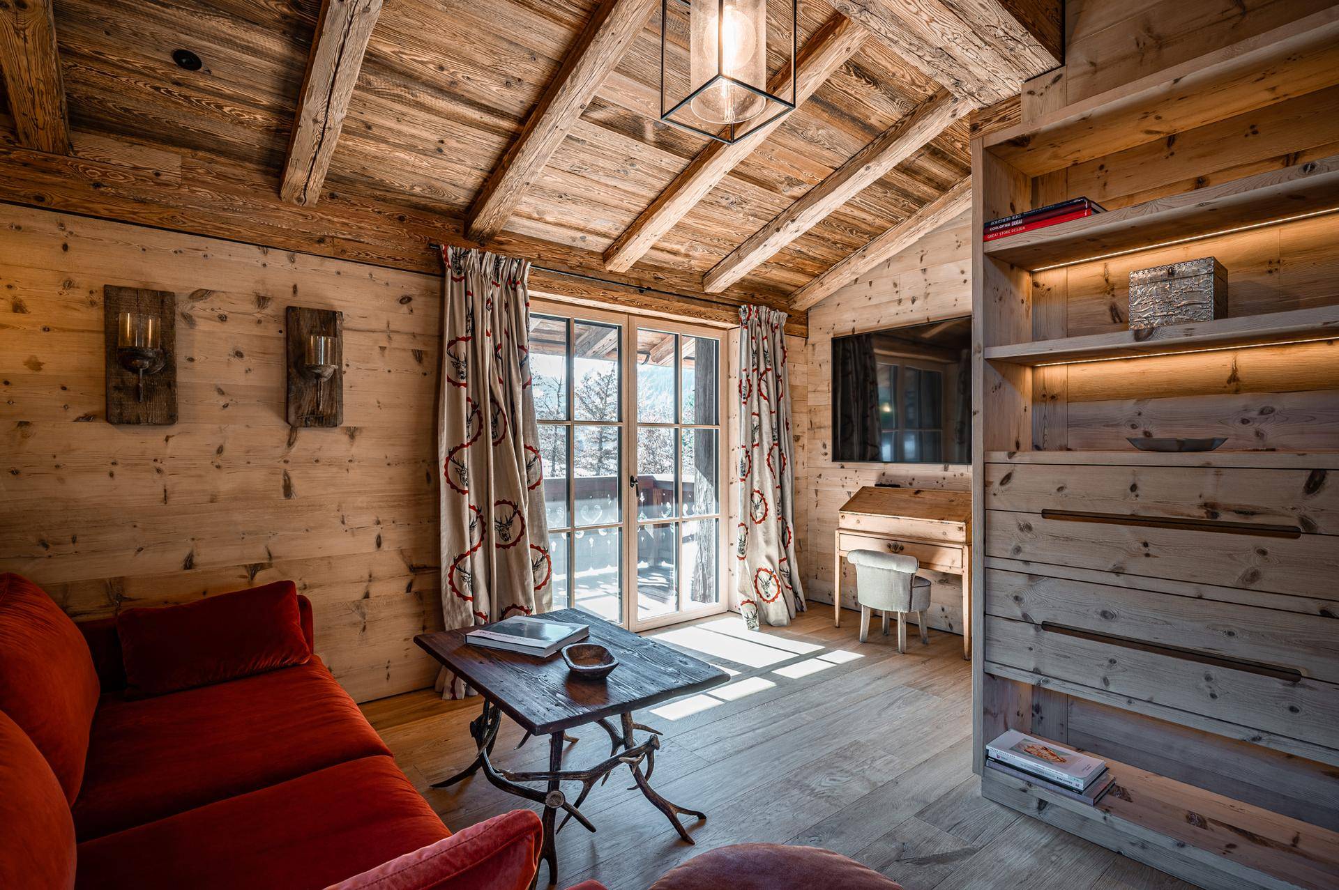 Gemütliches Schlafzimmer im alpinen Stil mit Holzwänden, Dachschräge und Zugang zum Balkon.