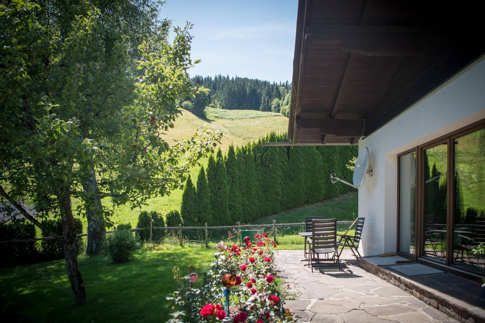 Gemütliche Steinterrasse mit Gartenmöbeln, Rosenbeeten und weitem Blick ins Grüne.