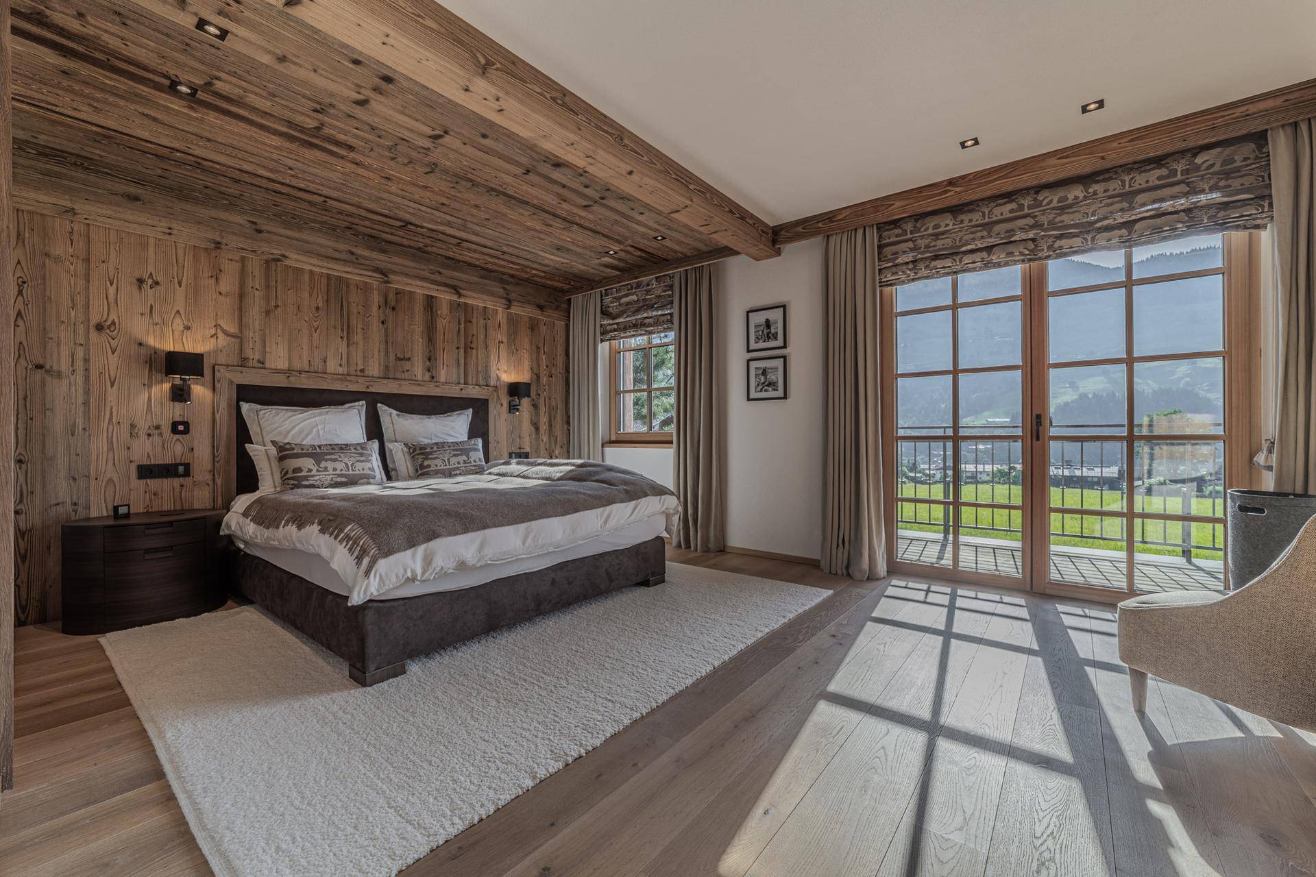 Helles Schlafzimmer im alpinen Stil mit Holzwänden, Balkonzugang und Panoramablick auf die Berge.