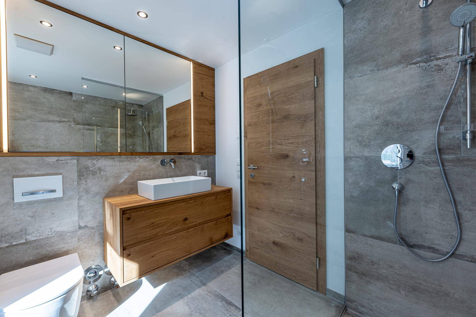Elegantes Badezimmer mit begehbarer Dusche, Holzwaschtisch und großem Spiegelschrank, modern gefliest.