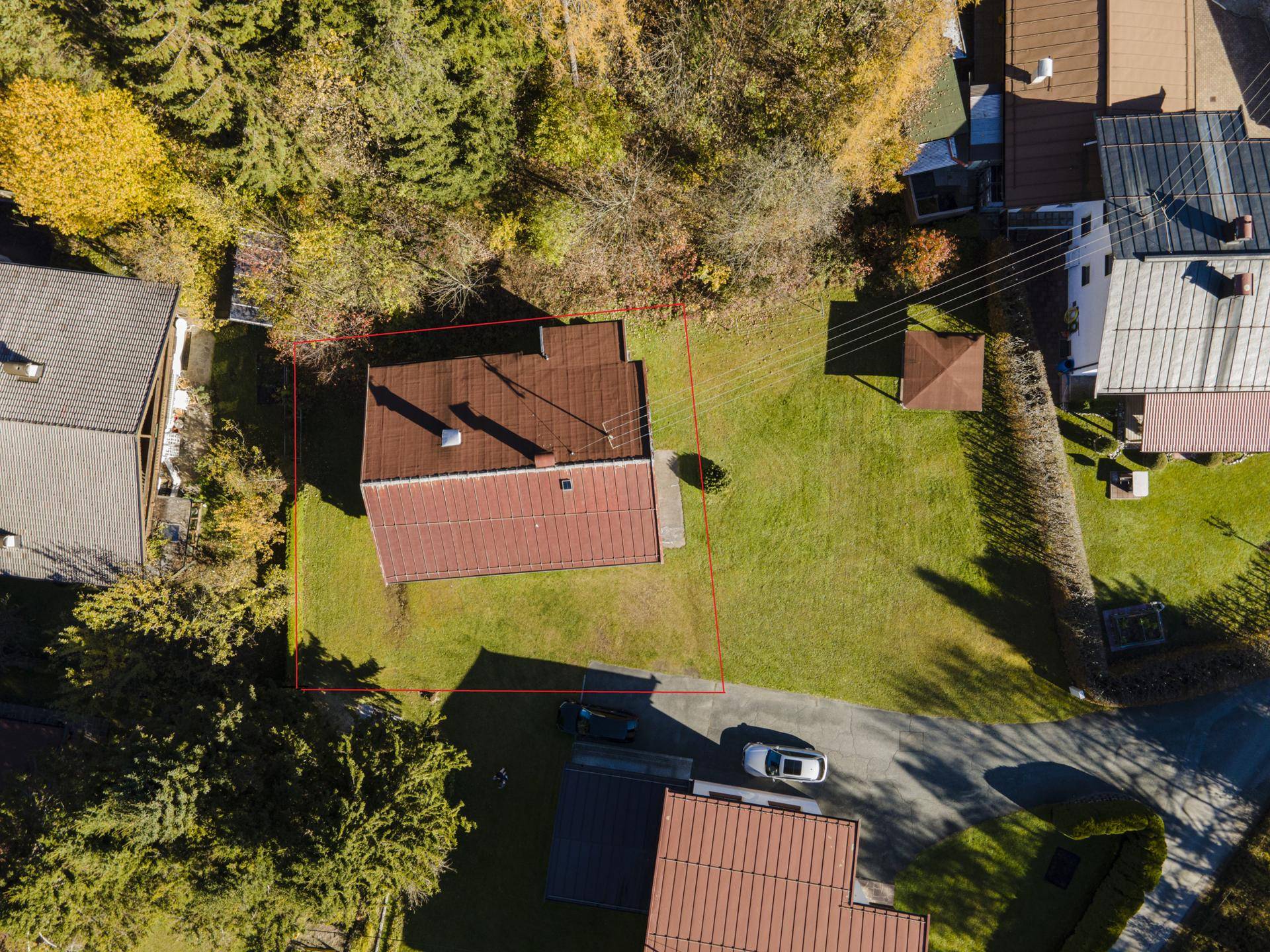 Luftaufnahme eines Hauses mit rotem Dach und großem Grundstück, umgeben von Bäumen und Nachbarhäusern.