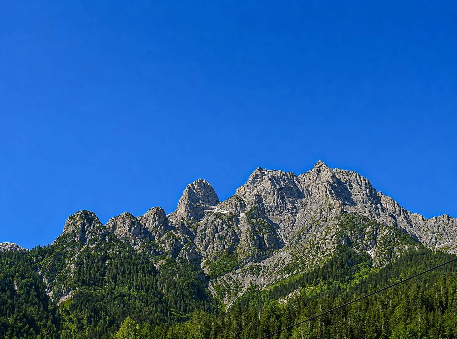 Imposante, zerklüftete Berggipfel mit grünen Wäldern an den unteren Hängen unter klarem Himmel.