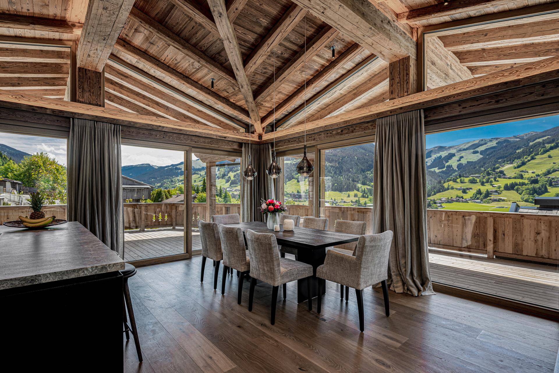 Eleganter Essbereich mit großem Holztisch, bequemen Stühlen und Panoramafenstern mit Bergblick.