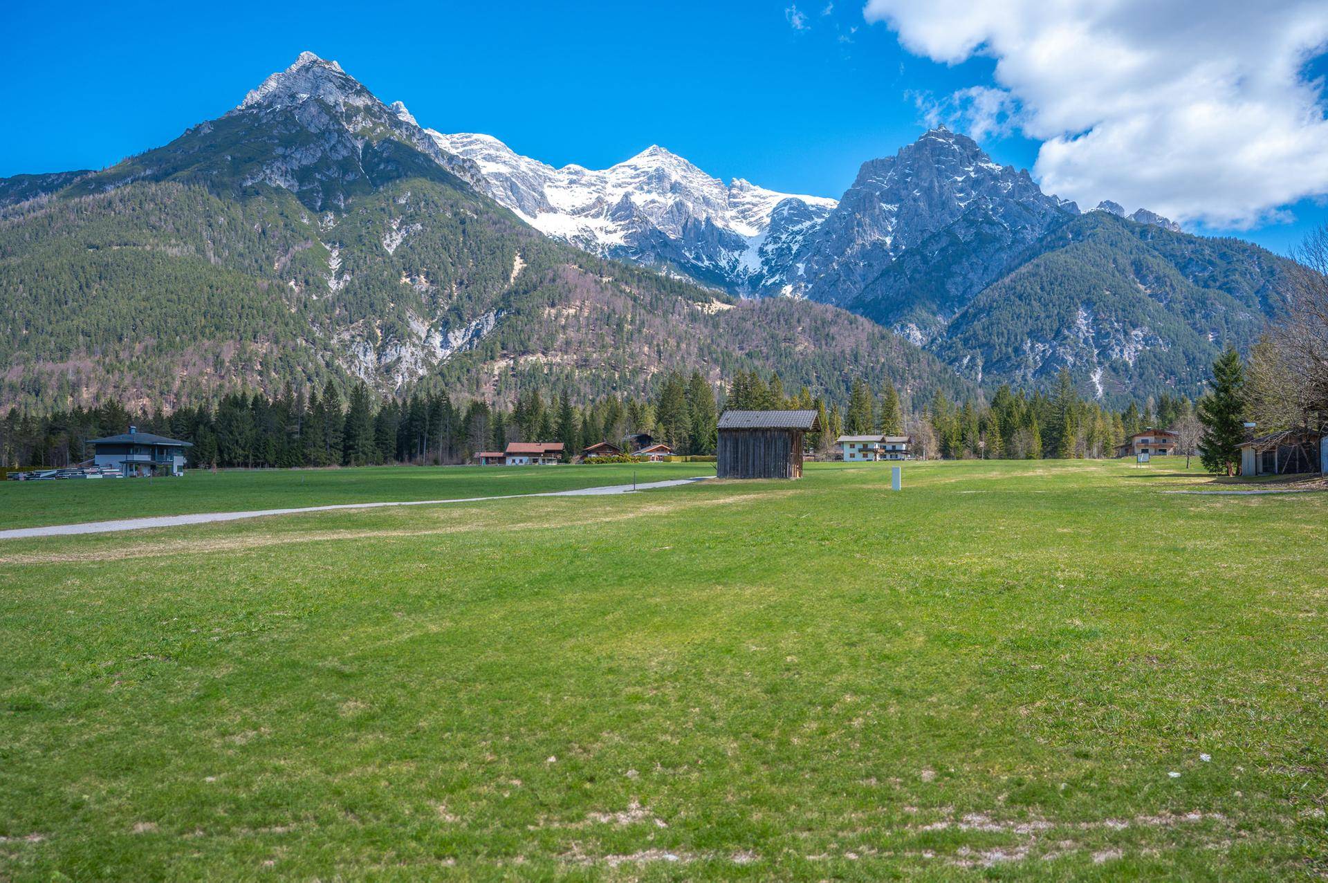 Idyllische Landschaft mit saftigen grünen Wiesen und imposanten Bergen am Horizont.