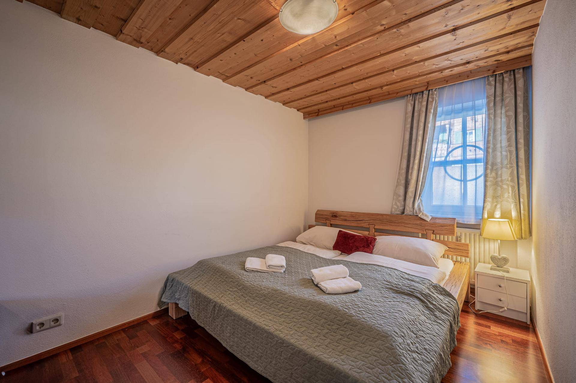 Schlafzimmer mit Holzbalkendecke, Holzboden und gemütlichem Doppelbett, strahlt eine warme Atmosphäre aus.