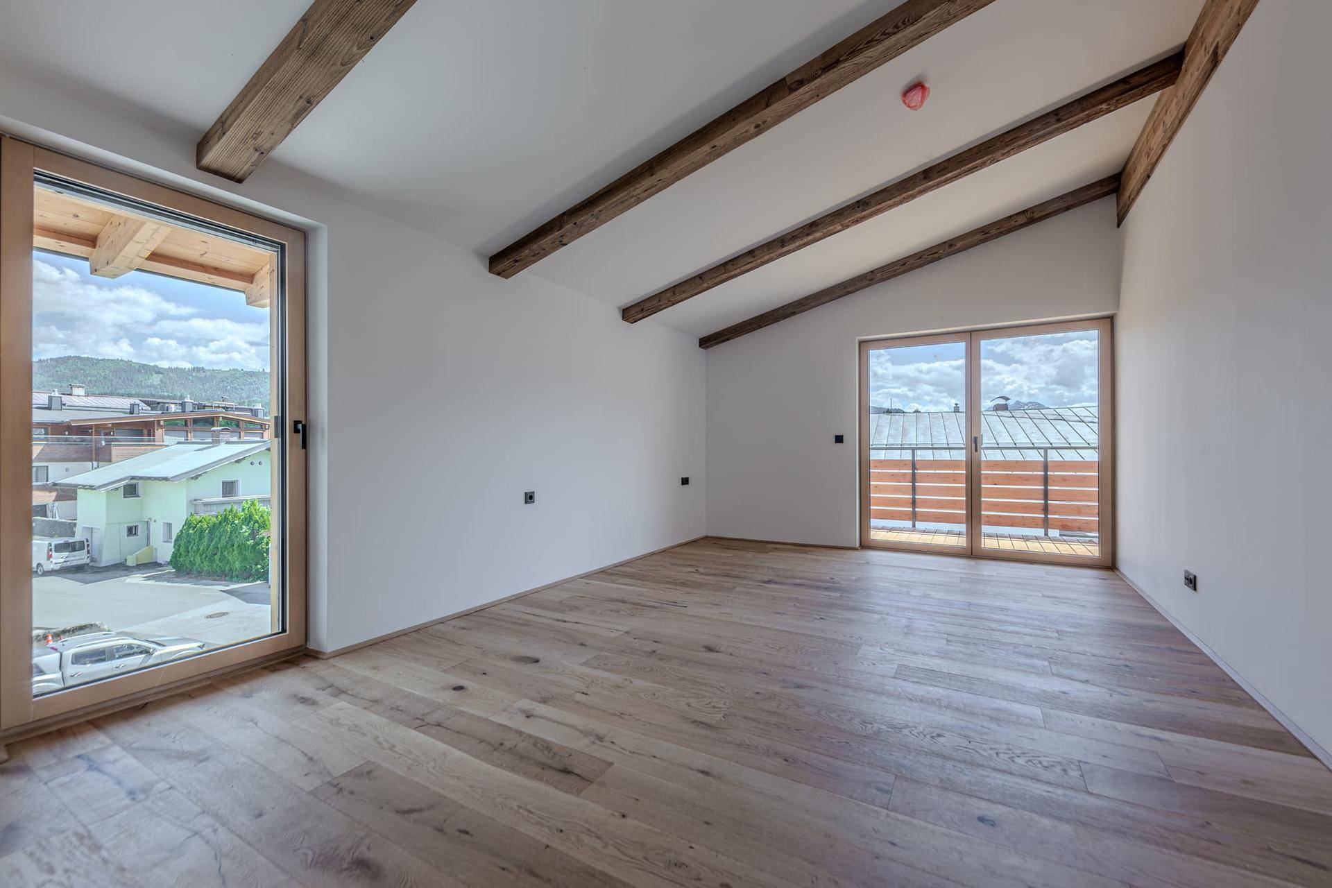 Helles Schlafzimmer mit Holzbalken, Holzboden und Zugang zu einem Balkon, bietet einen Blick auf die Umgebung.