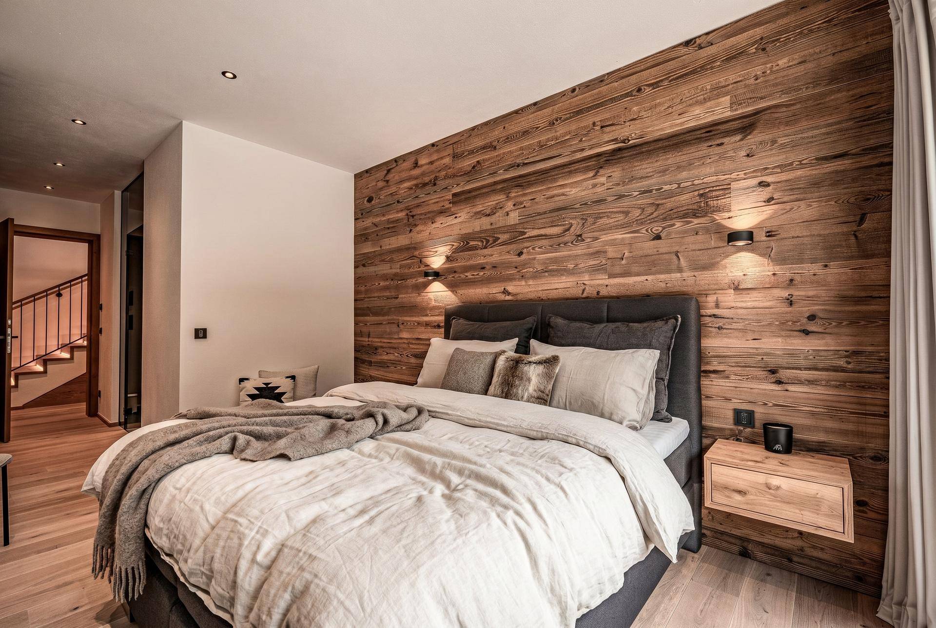 Stilvolles Schlafzimmer mit Holzakzentwand, großem Bett und Zugang zu einem Treppenhaus.