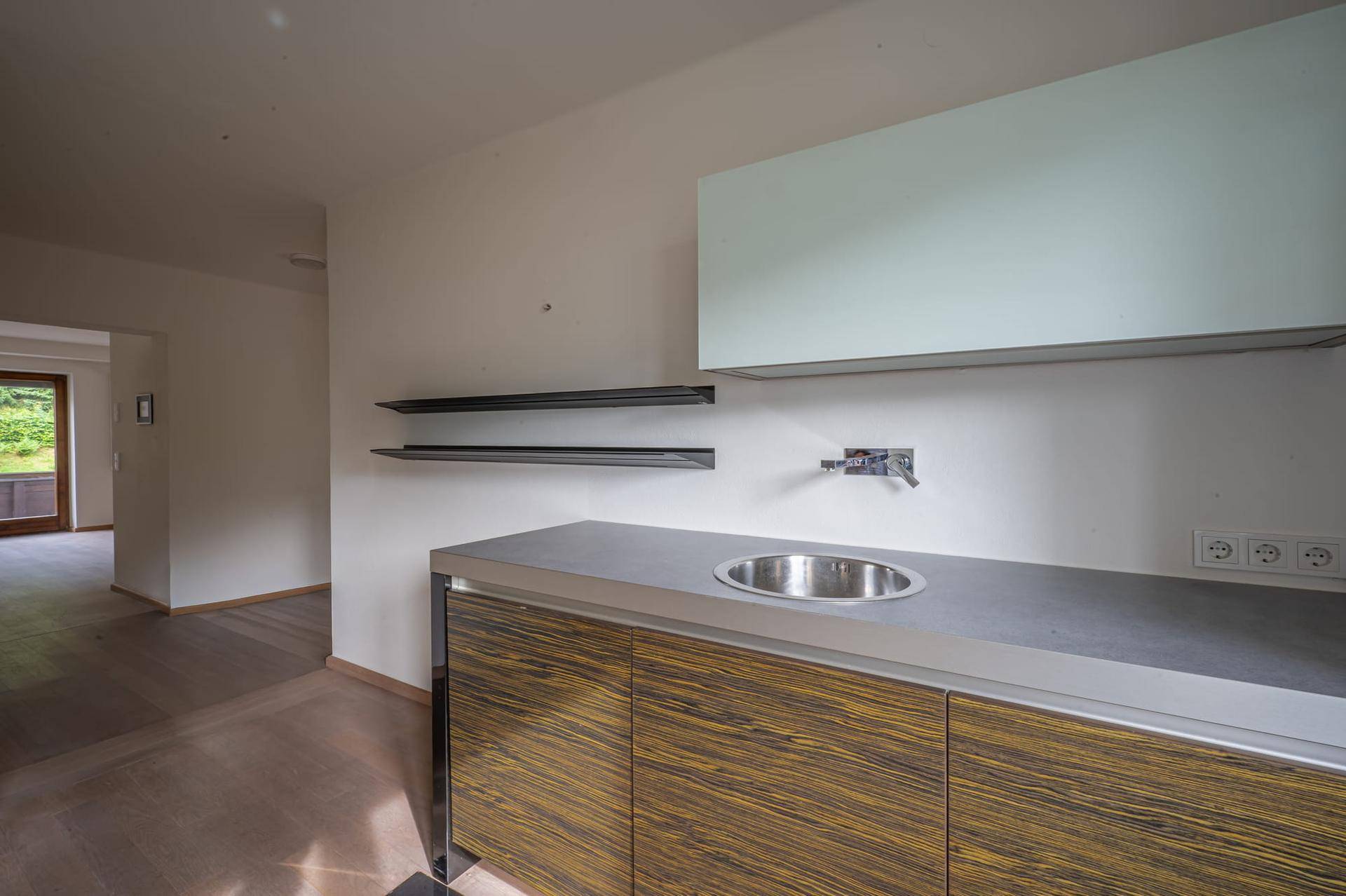 Moderne Küchenzeile mit Spülbecken, Holzschränken, grauer Arbeitsplatte und schwebenden Wandregalen.