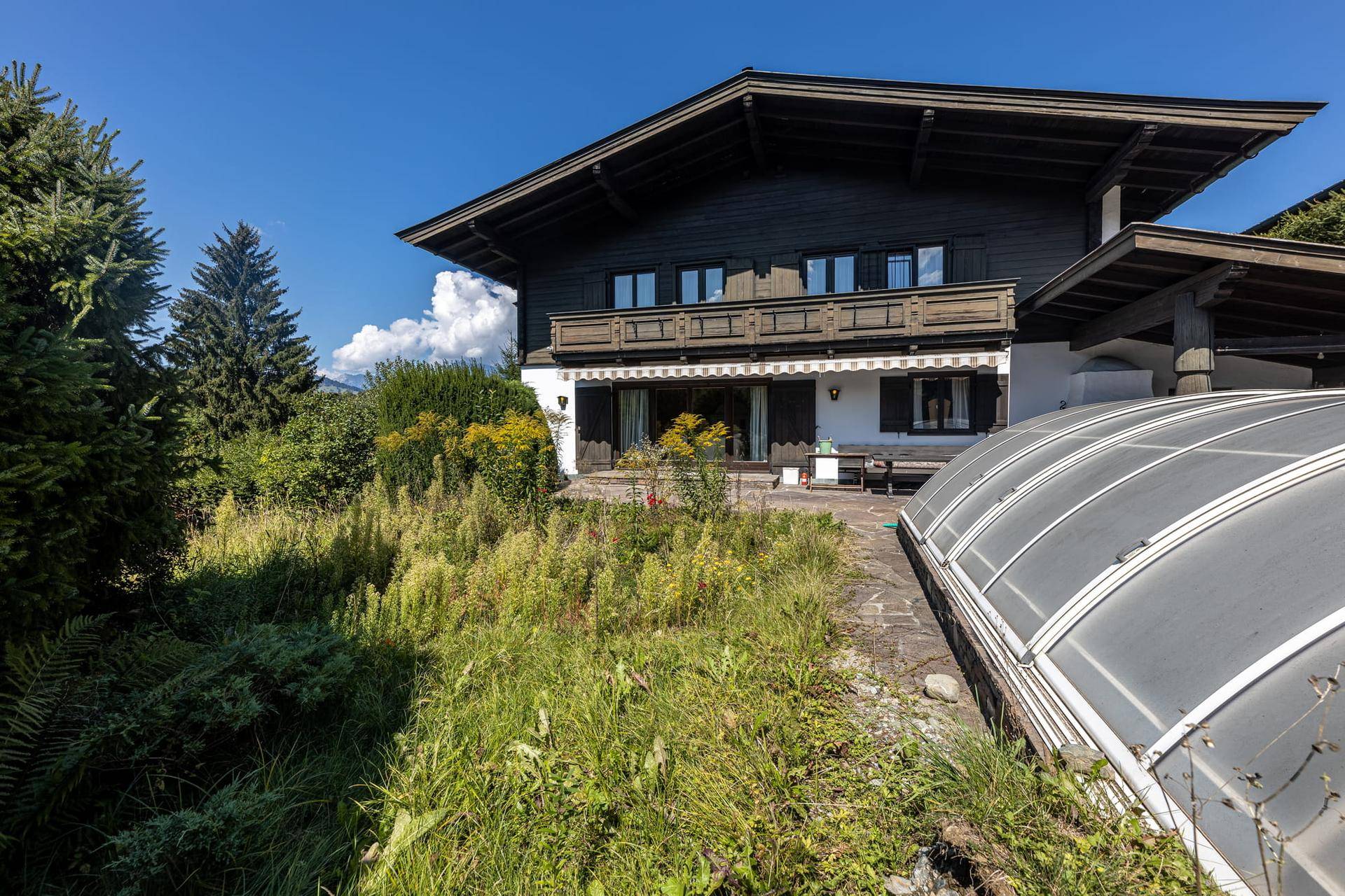 Rückseite des Hauses mit Gartenbereich, überdachtem Pool und Balkon im Obergeschoss.