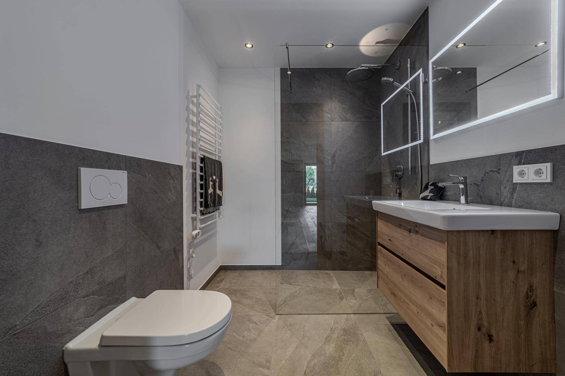 Modernes Badezimmer mit dunklen Fliesen, einer begehbaren Dusche und einem stilvollen Holzwaschtisch.