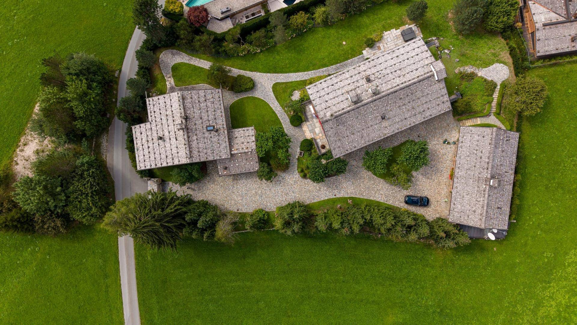 Draufsicht auf mehrere Chalets mit geschwungenen Zufahrten und üppiger grüner Umgebung.