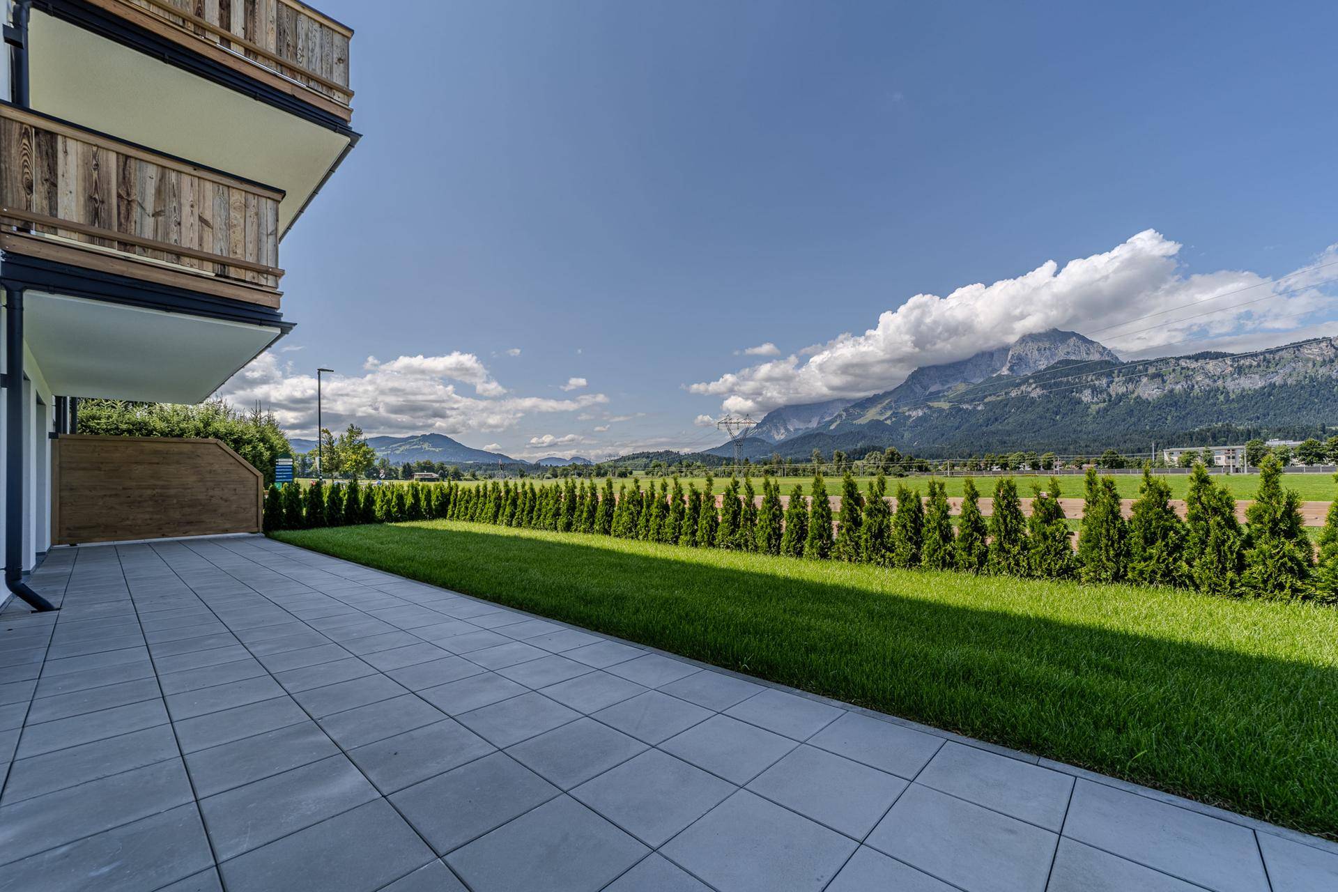 Geräumige Terrasse mit grauen Fliesen, angrenzendem Rasen und einem weiten Blick auf die umliegende Berglandschaft.