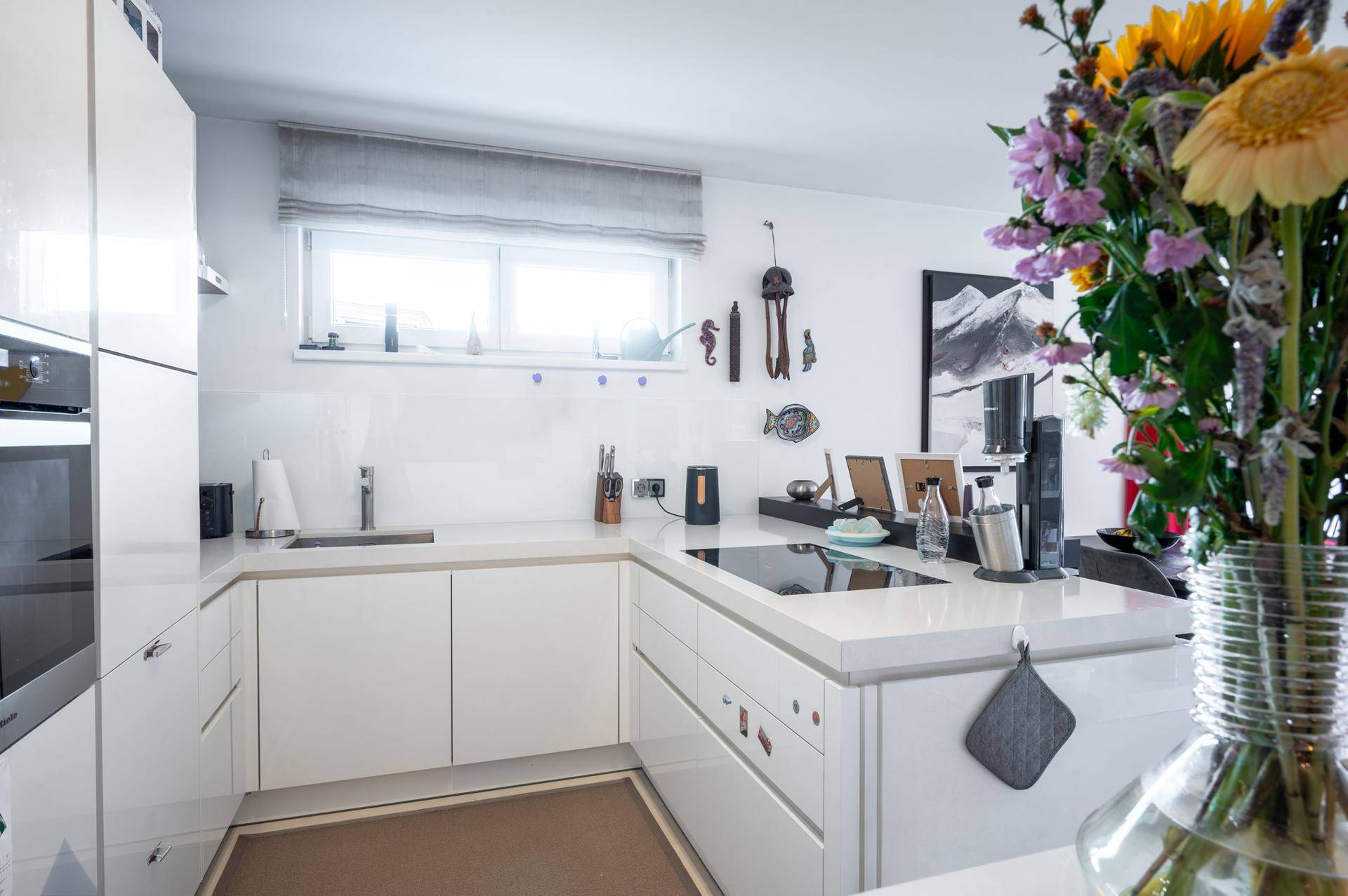 Helle, moderne Einbauküche in Weiß mit Induktionskochfeld und Fenster für viel Tageslicht.